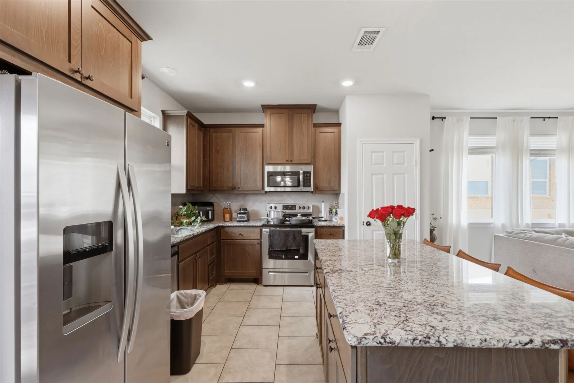 Kitchen featuring a large island with a patterned countertop, rich wood-finish cabinetry, stainless steel appliances, and light-toned tile flooring