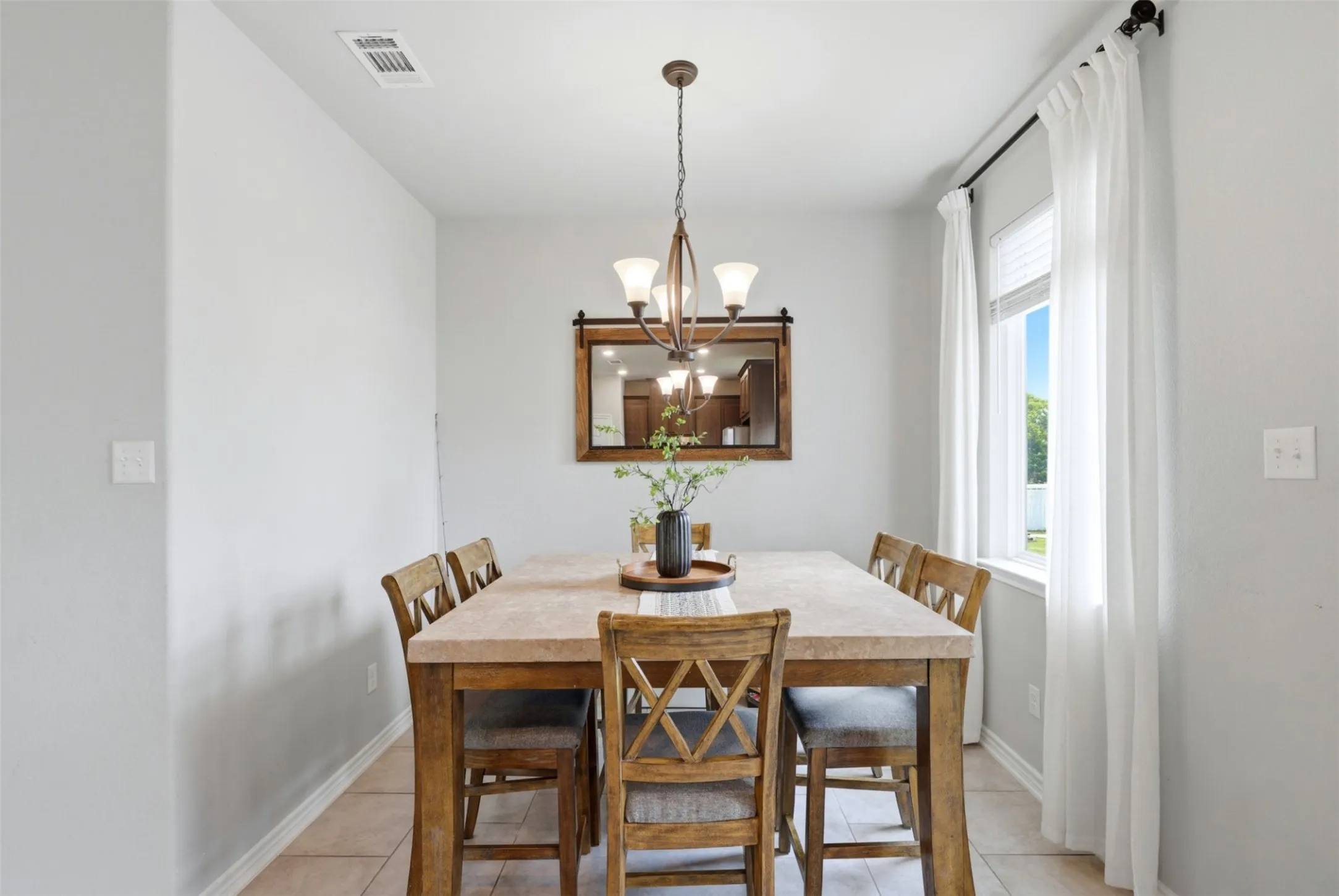 Dining area with a window, white curtains, and a rectangular mirror with a barn door inspired frame