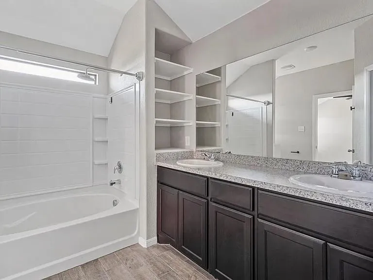 Bathroom featuring a dual vanity with a speckled countertop, integrated sinks, dark wood-finish cabinetry, and a full-width mirror