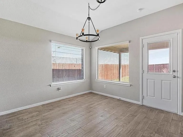 Dining area featuring wood-finish flooring, two windows with blinds, a side-light exterior door, and an overhead chandelier