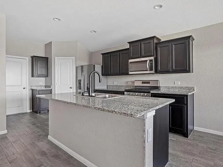 Kitchen featuring a large island with a sink, granite countertops, dark wood-finish cabinetry, stainless steel appliances, and wood-finish flooring