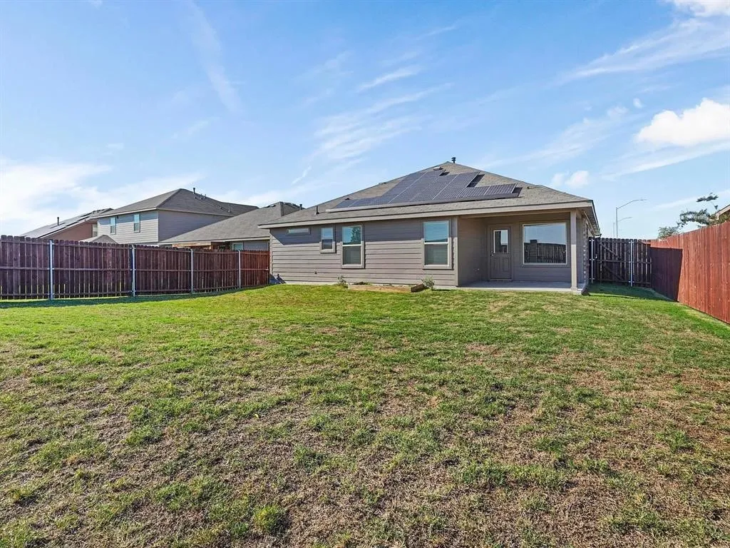 Spacious backyard featuring a sloped lawn, a full wooden privacy fence, and a covered patio area