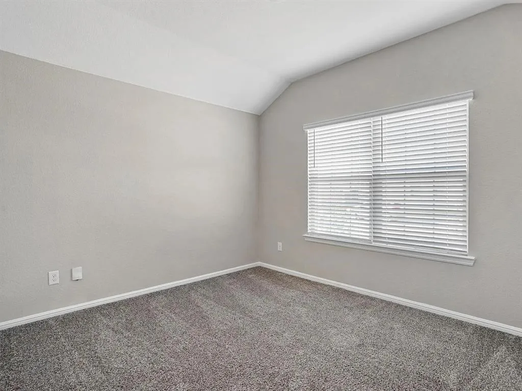 Interior room featuring sloped ceilings, a window with blinds, light gray wall paint, white trim, and gray carpet