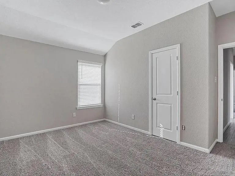 Carpeted room featuring a single window with blinds, a white paneled door, and neutral gray walls
