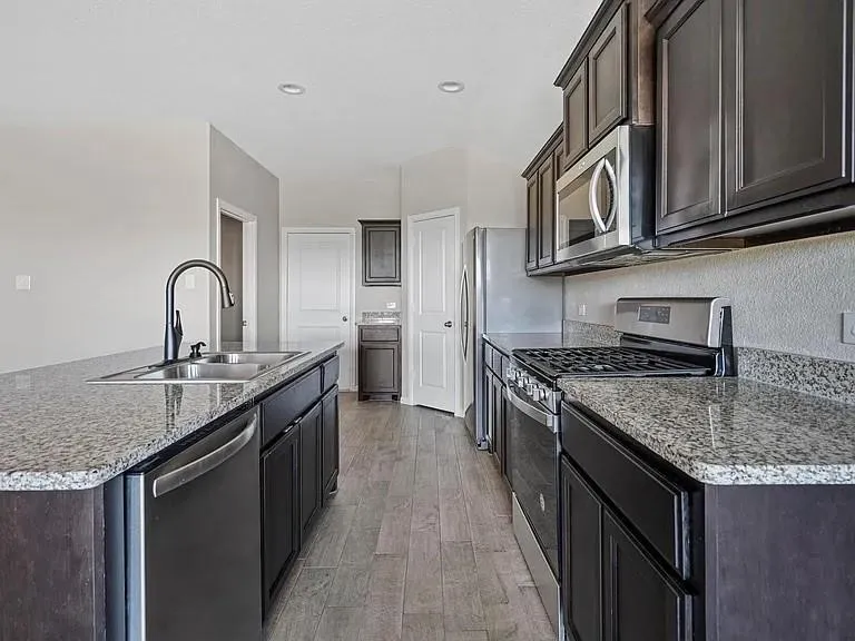 Modern kitchen featuring dark wood cabinetry, granite countertops, stainless steel appliances, and wood-finish flooring