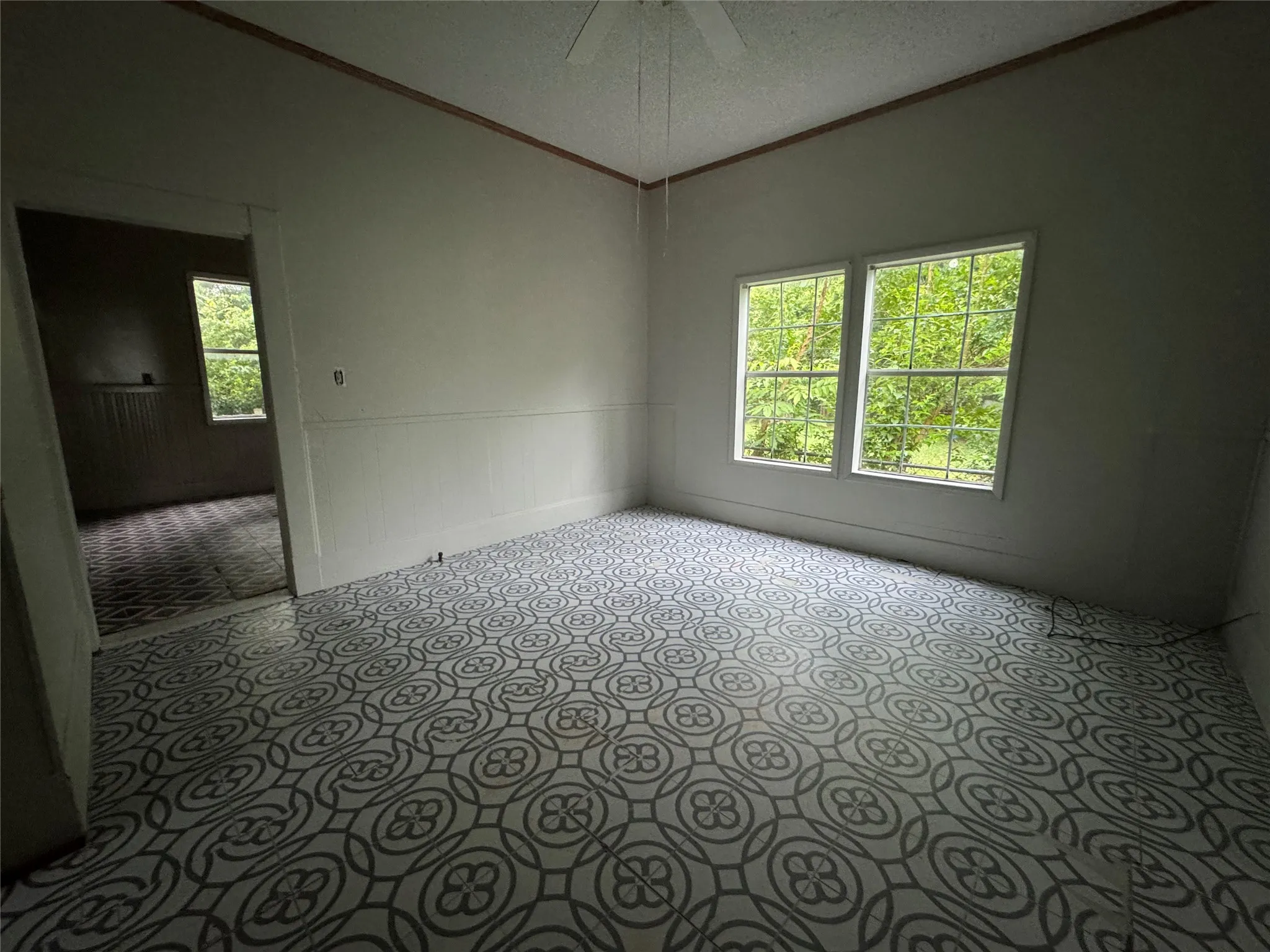 Spacious room featuring patterned flooring, white walls with wainscoting, and large double windows providing natural light