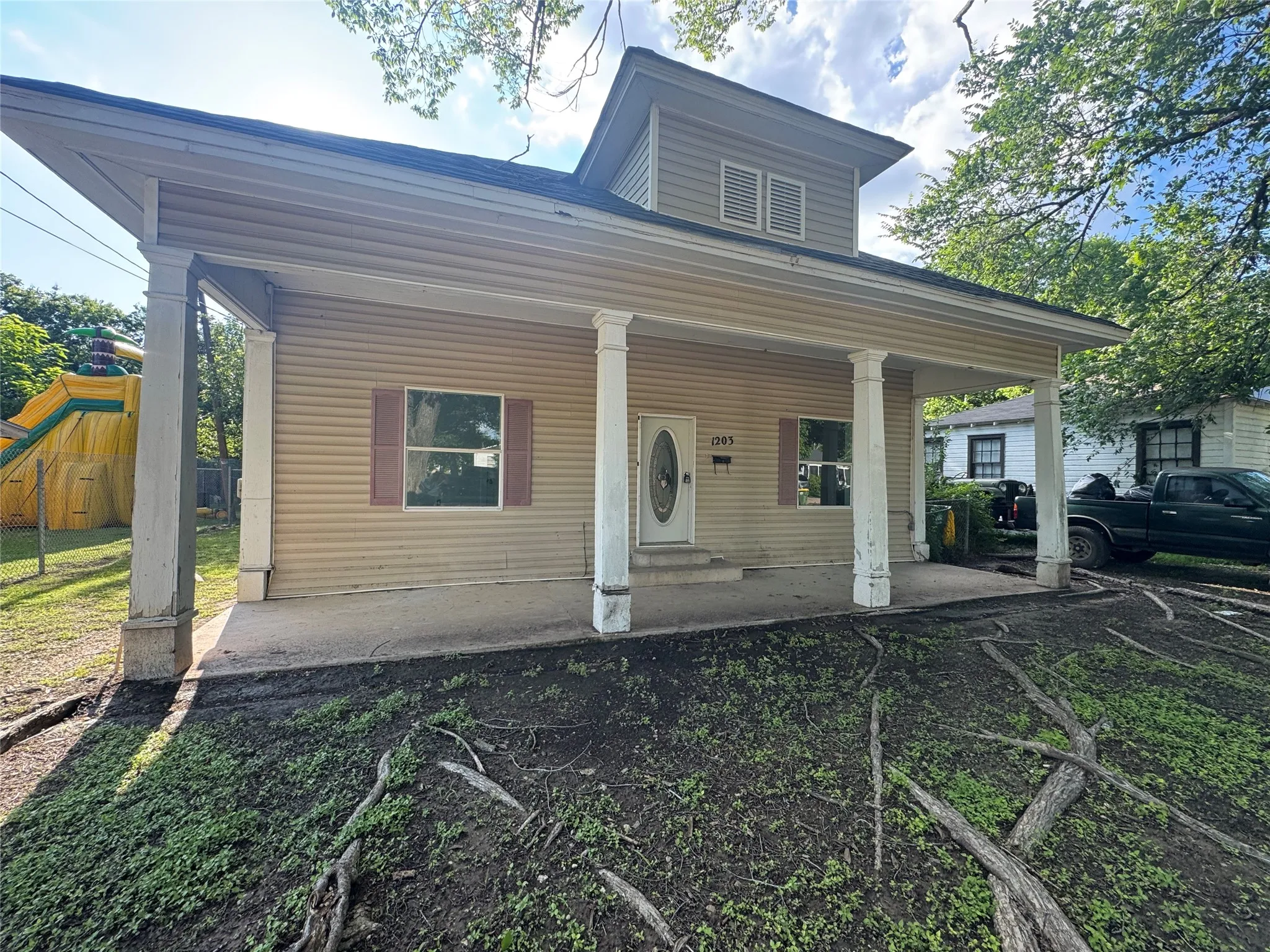 Covered front porch with classic columns, horizontal siding facade, upper-level dormer with louvered vents, and a prominent front door with oval glass insert