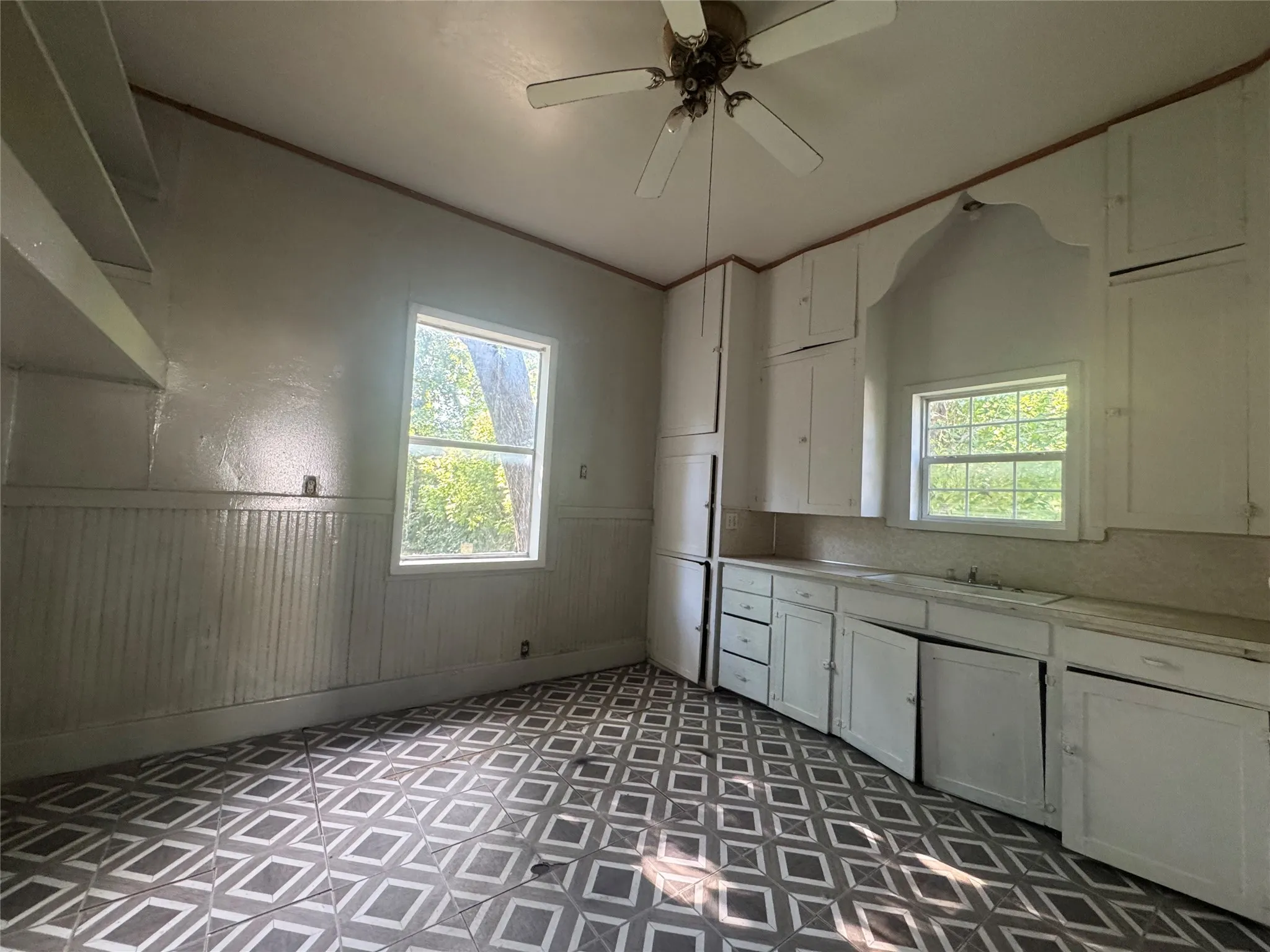 Kitchen featuring patterned floor tiles, white wainscoting, and white cabinetry