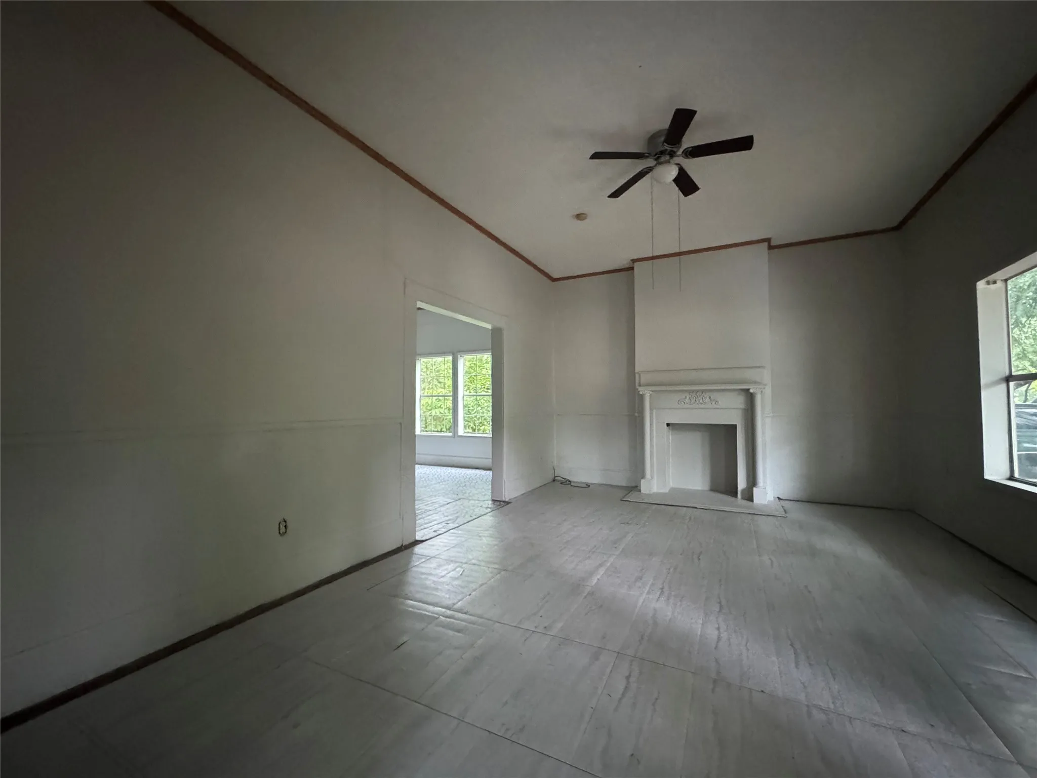 Spacious room featuring a decorative fireplace with a mantel, ceiling fan, and crown molding