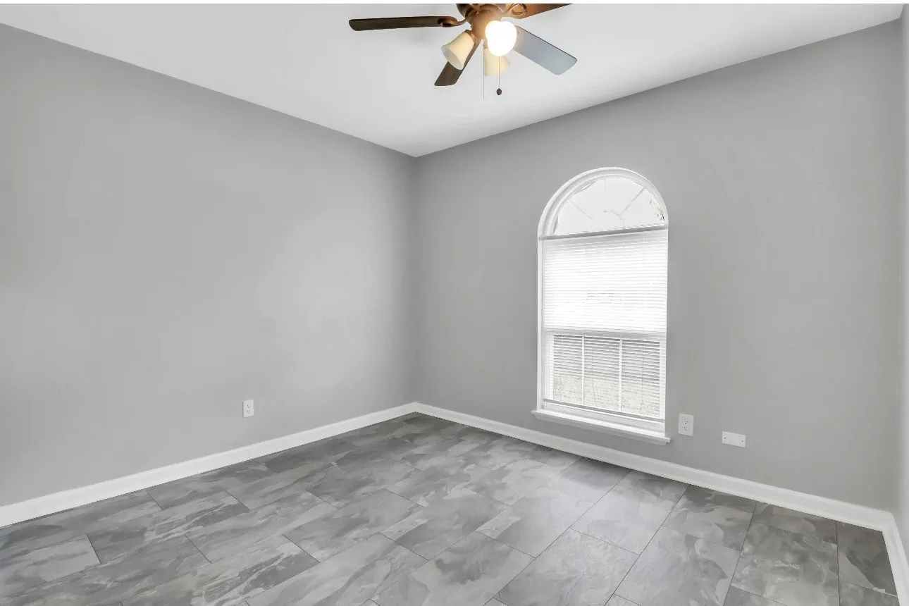 Room featuring a prominent arched window, grey wall paint, wood-finish flooring, white baseboards, and a ceiling fan with integrated lighting