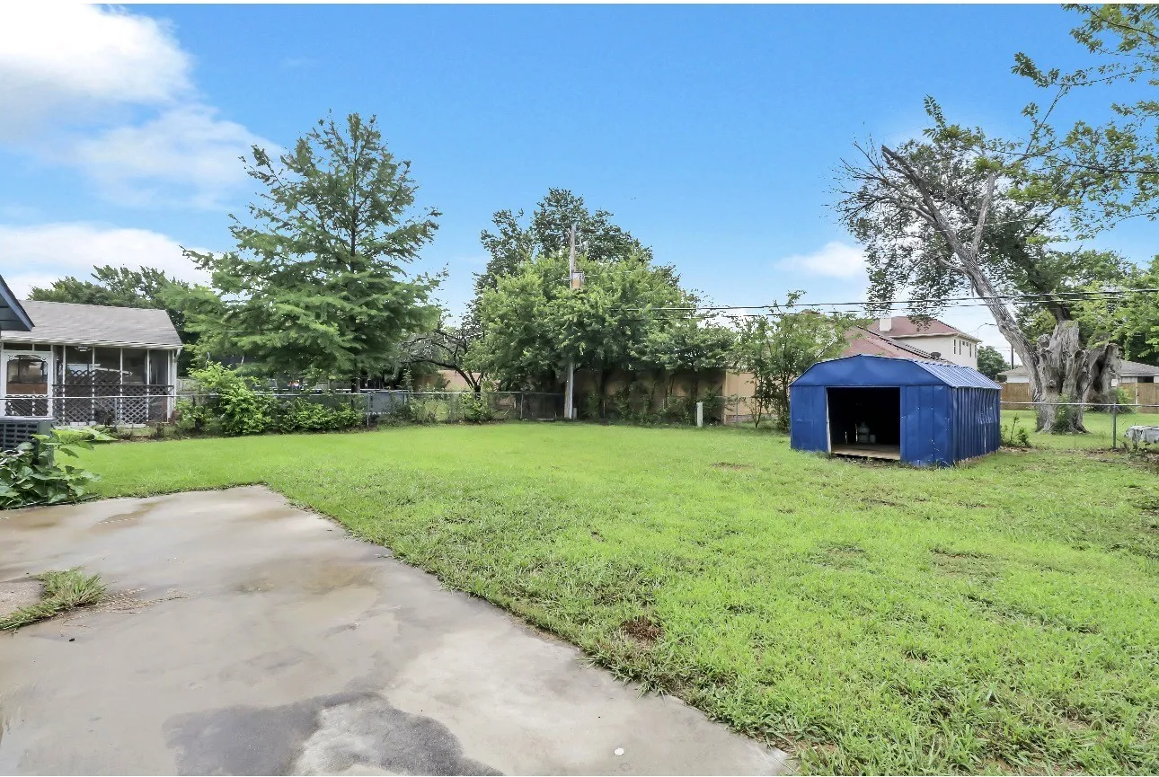 Expansive backyard featuring a concrete patio, a blue metal shed, and a screened porch