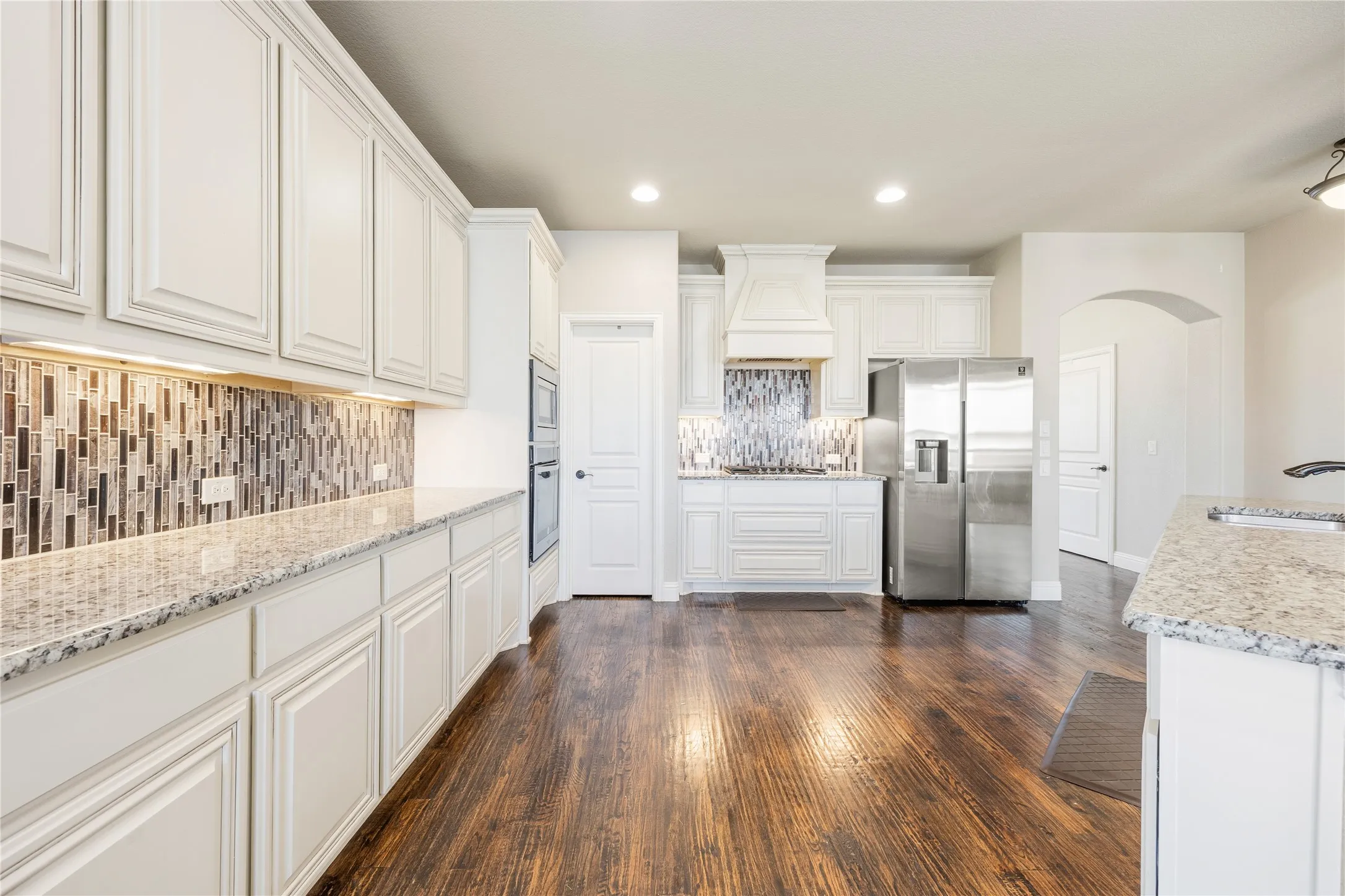 Kitchen featuring wood-finish flooring, white cabinetry, speckled countertops, stainless steel appliances, and a mosaic tile backsplash