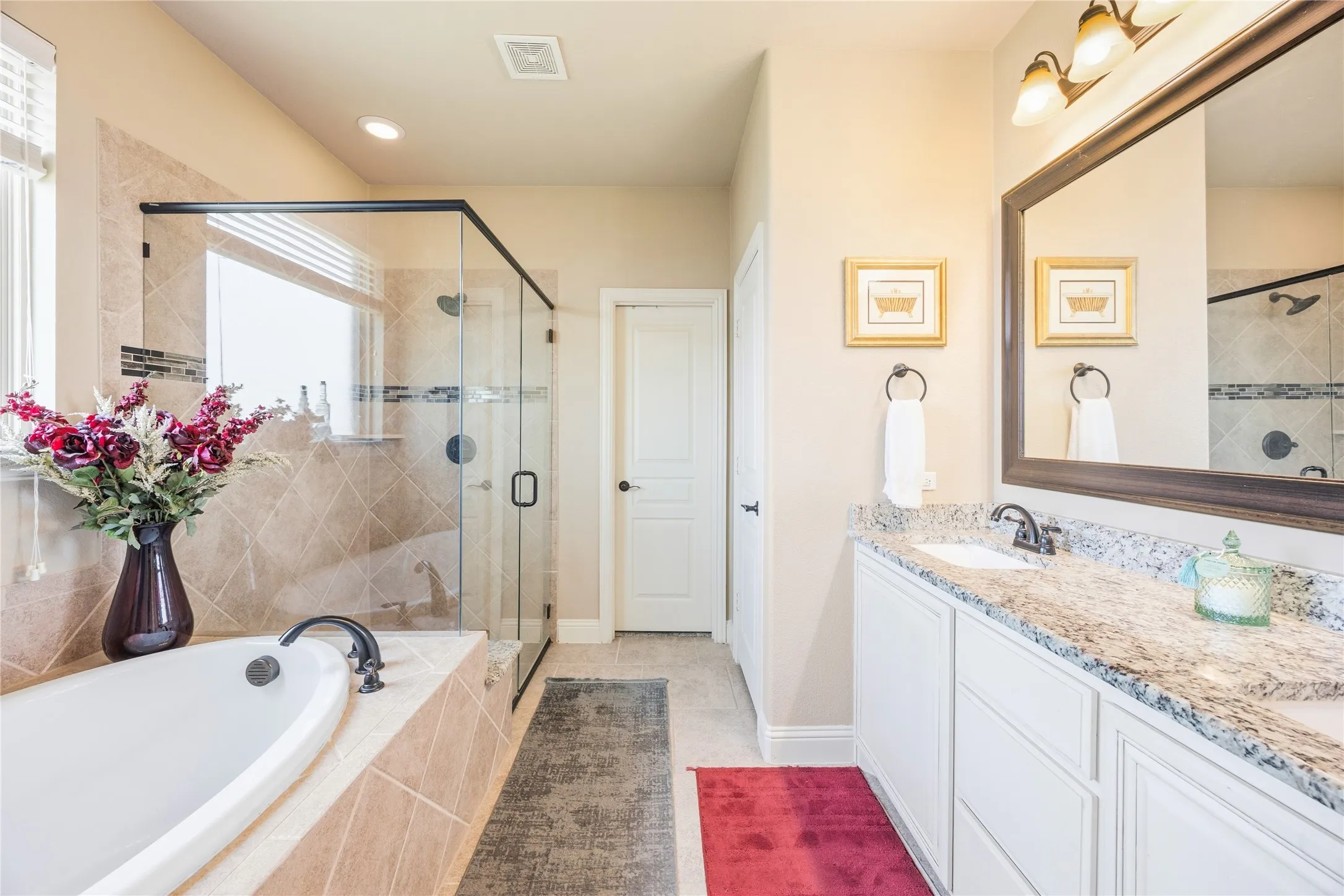 Bathroom featuring a built-in soaking tub with tiled surround, a glass-enclosed shower with tiled walls and dark bronze fixtures, and a double vanity with a light-toned countertop, undermount sinks, and dark bronze faucets