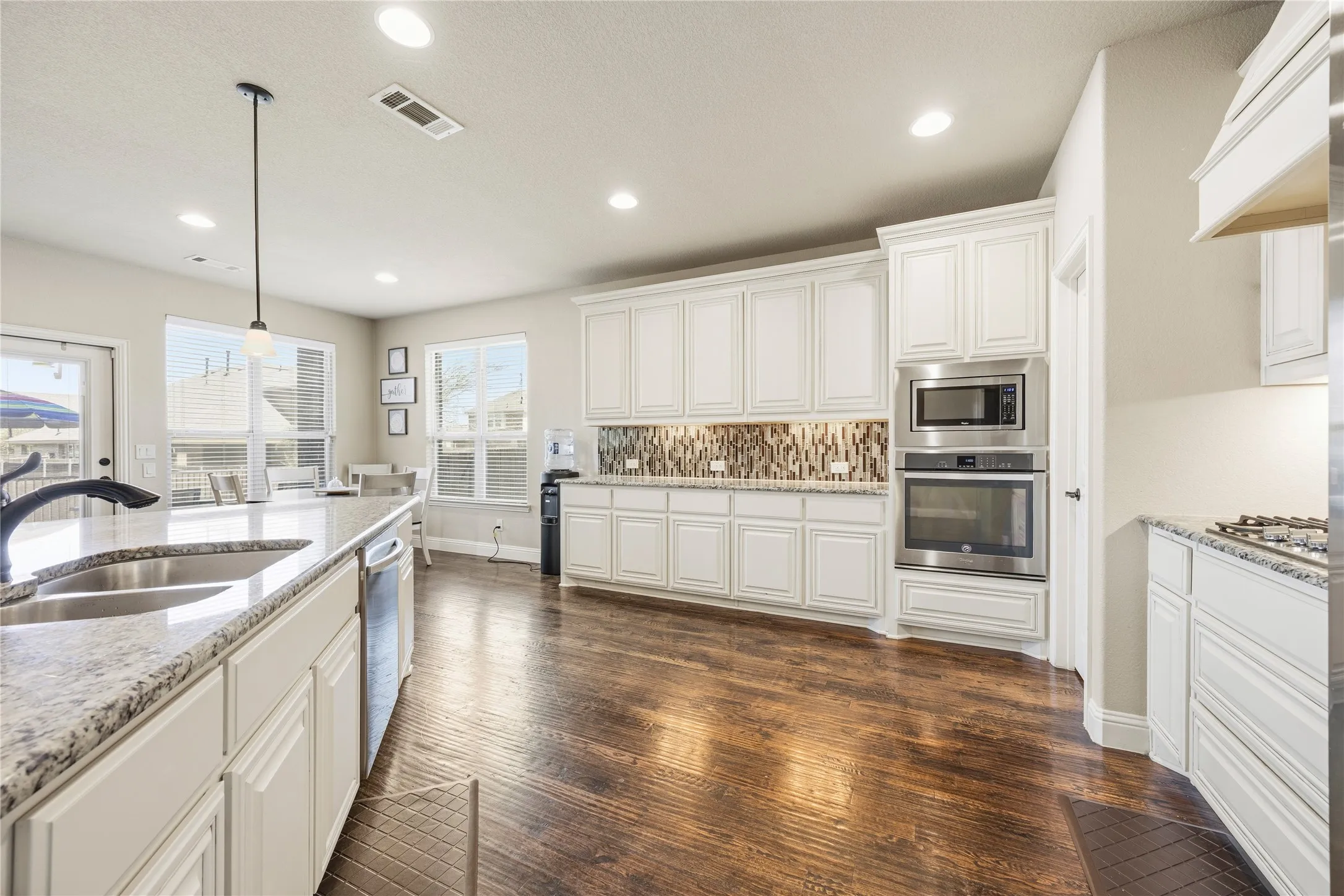 Gourmet kitchen featuring white cabinetry, granite countertops, built-in stainless steel appliances, wood-finish flooring, and a decorative tile backsplash
