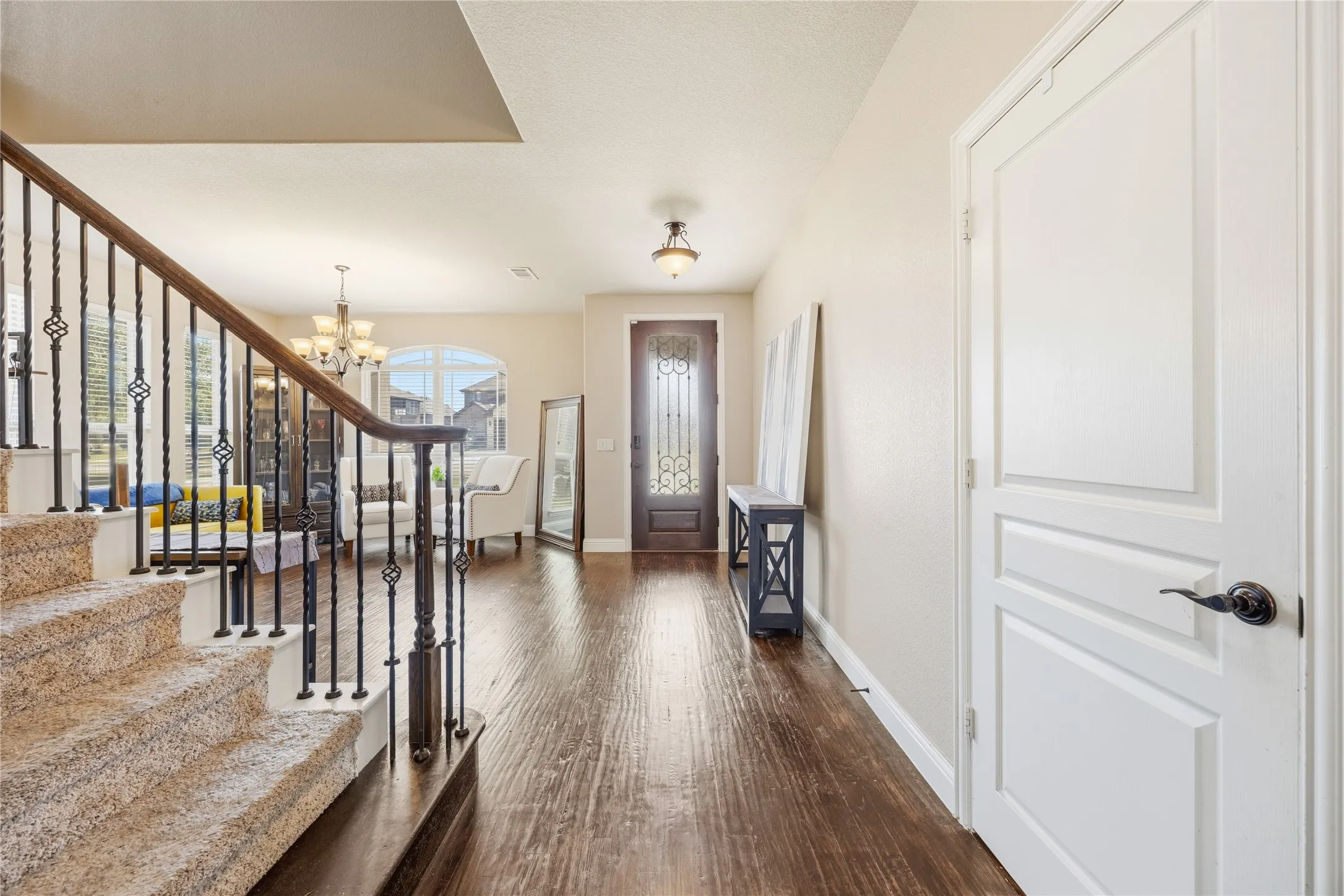 Foyer featuring rich wood-finish flooring, a decorative glass-paneled entry door, and a carpeted staircase with wrought iron balusters