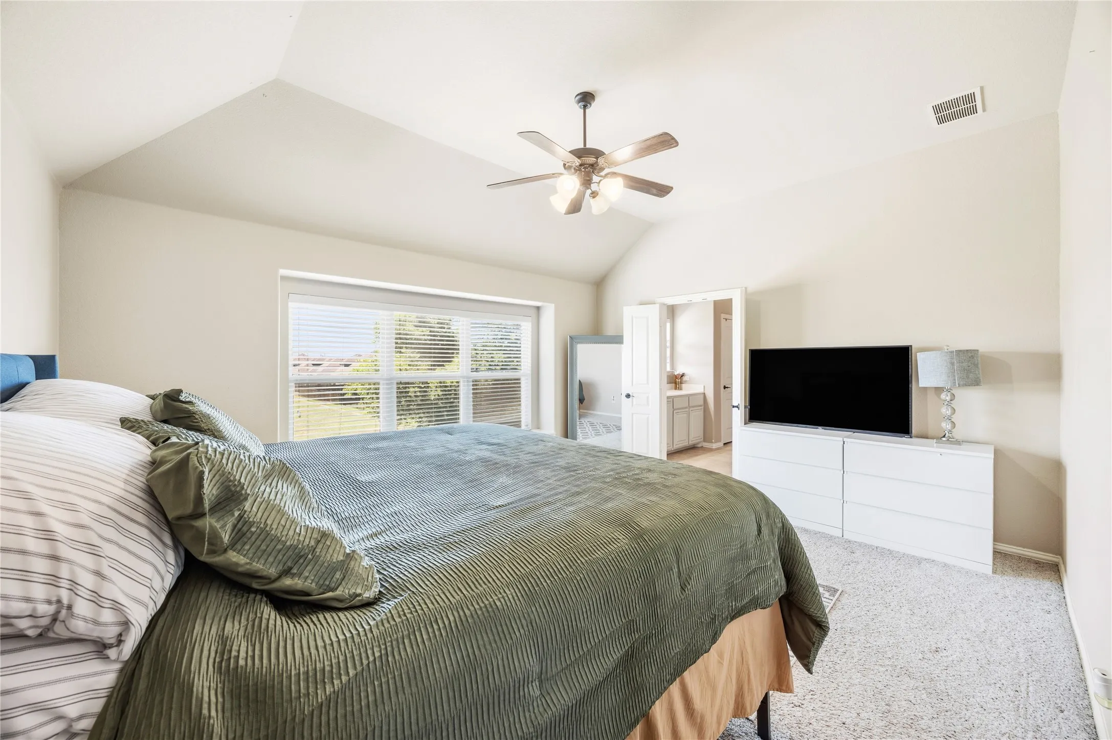 2nd floor Primary bedroom two suite. Vaulted ceiling with ceiling fan, large window with blinds, light-colored carpet flooring, and an open doorway to an interior space private full bathroom.