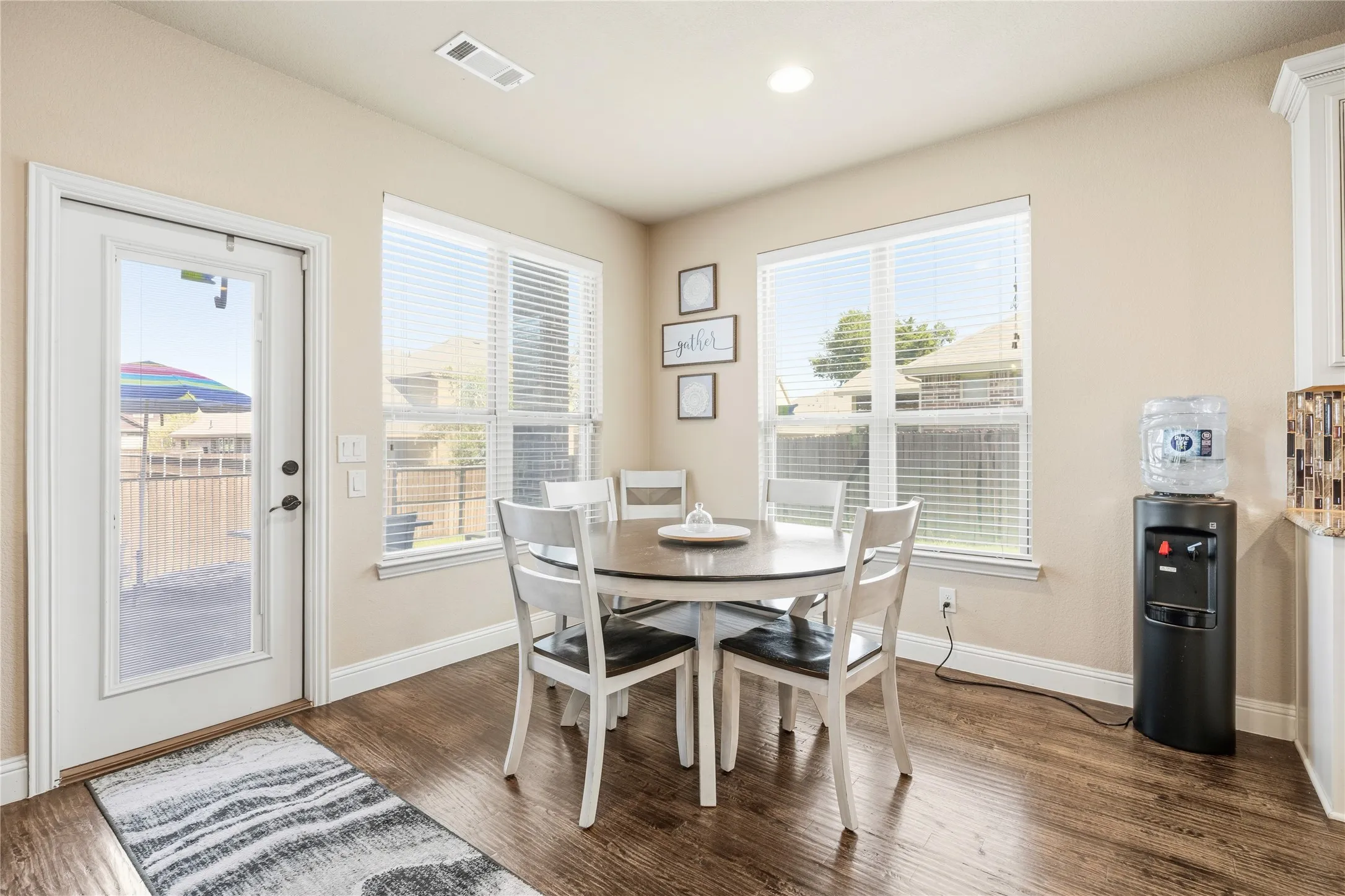 Dining area featuring wood-finish flooring, two large windows with blinds, and a white door with a glass panel