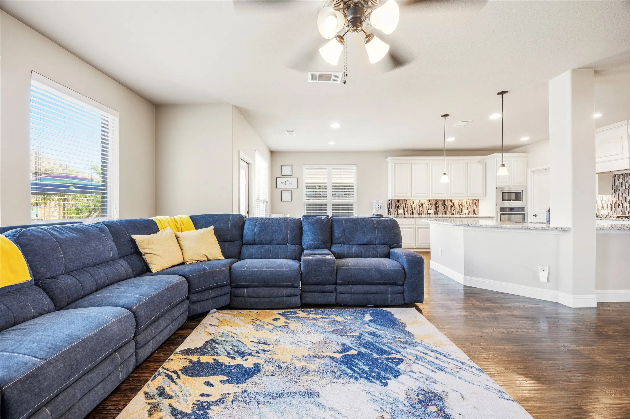 Open-concept living area featuring wood-finish flooring, a ceiling fan with integrated lighting, and multiple windows