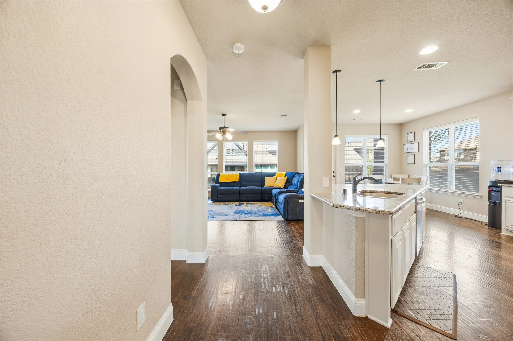 Open-concept interior featuring wood-finish flooring, a kitchen island with pendant lighting, recessed lighting, and an arched doorway