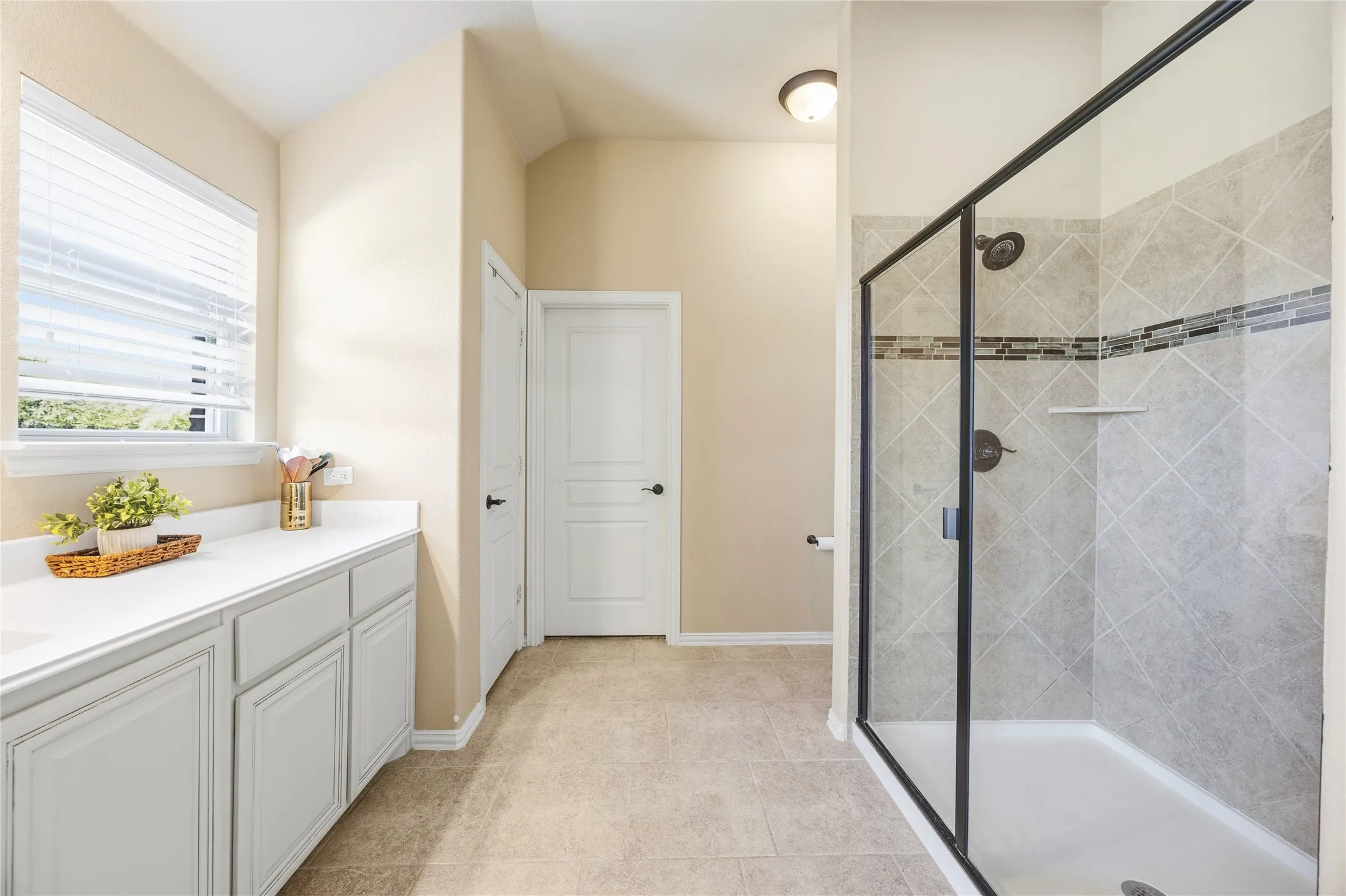 Spacious 2nd floor primary bathroom featuring a glass-enclosed shower with tile surround and decorative accent band with sink and spacious countertop space.