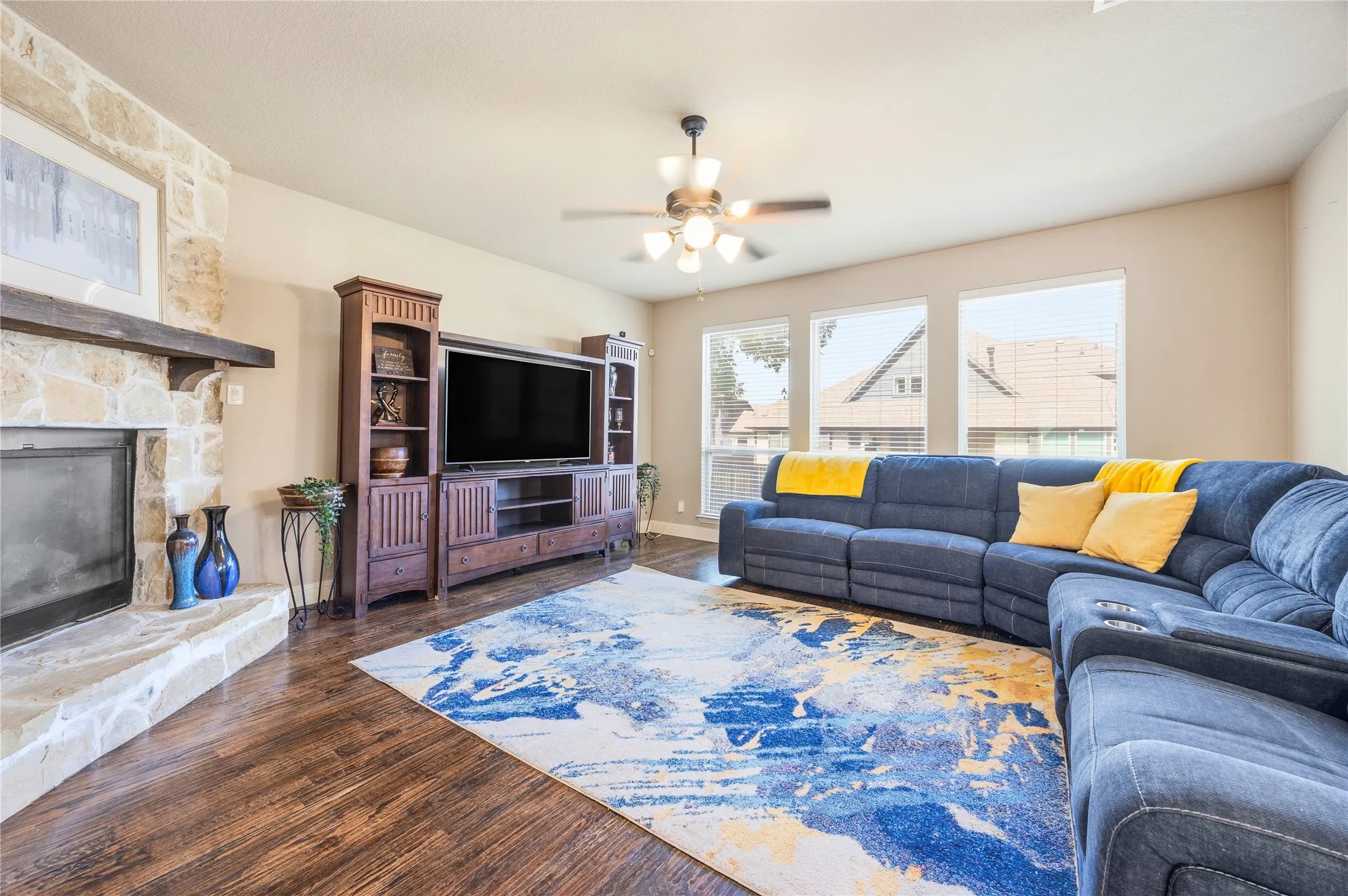 Spacious living area featuring a stone fireplace with a wood mantle, wood-finish flooring, and a ceiling fan with integrated lighting