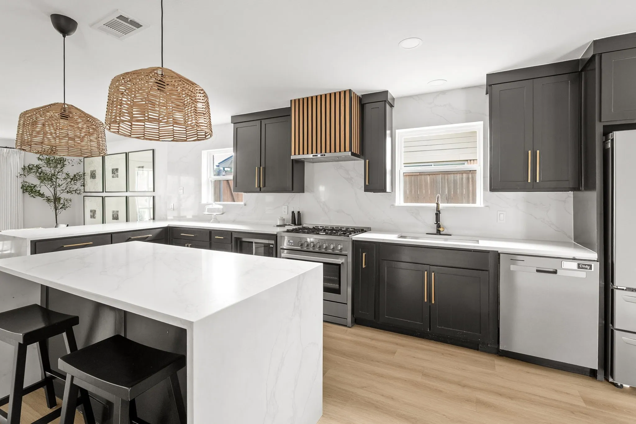 Modern kitchen featuring dark cabinetry with gold-tone hardware, white countertops, a large center island, wood-finish flooring, and stainless steel appliances
