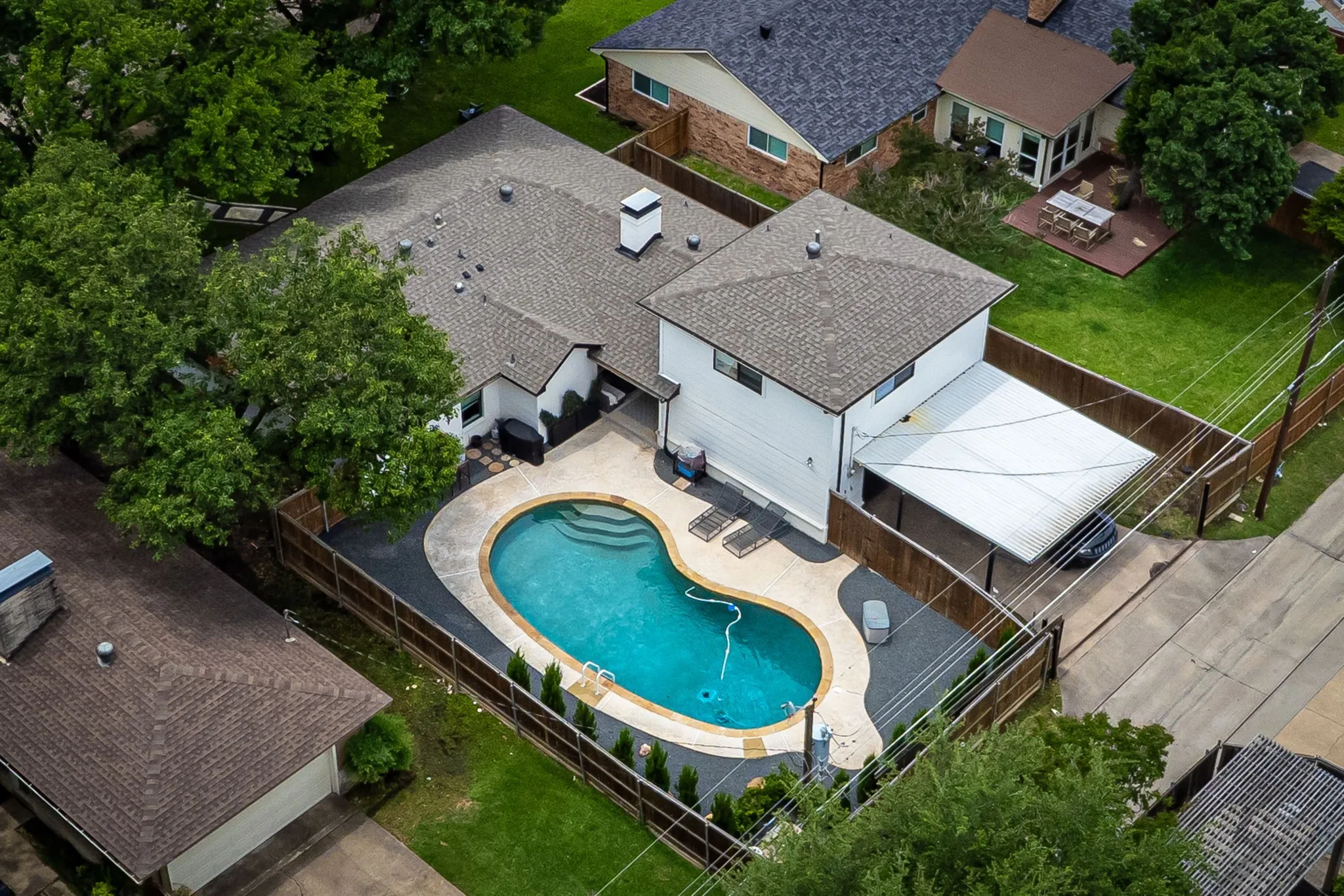 Private backyard featuring a freeform swimming pool with integrated steps, surrounding concrete decking, and perimeter fencing