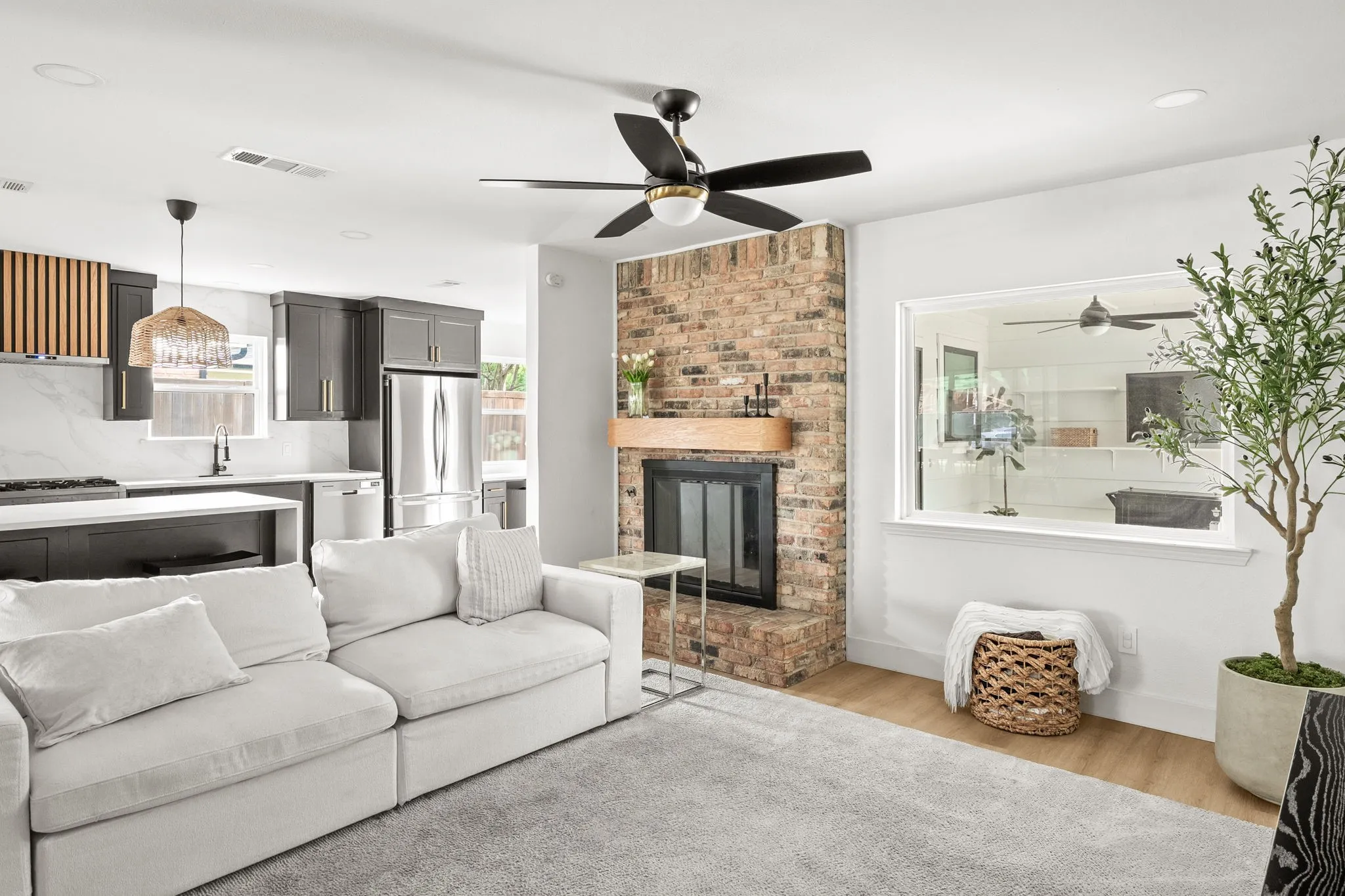 Open-concept living space with a brick fireplace, wood-finish mantel, and a ceiling fan