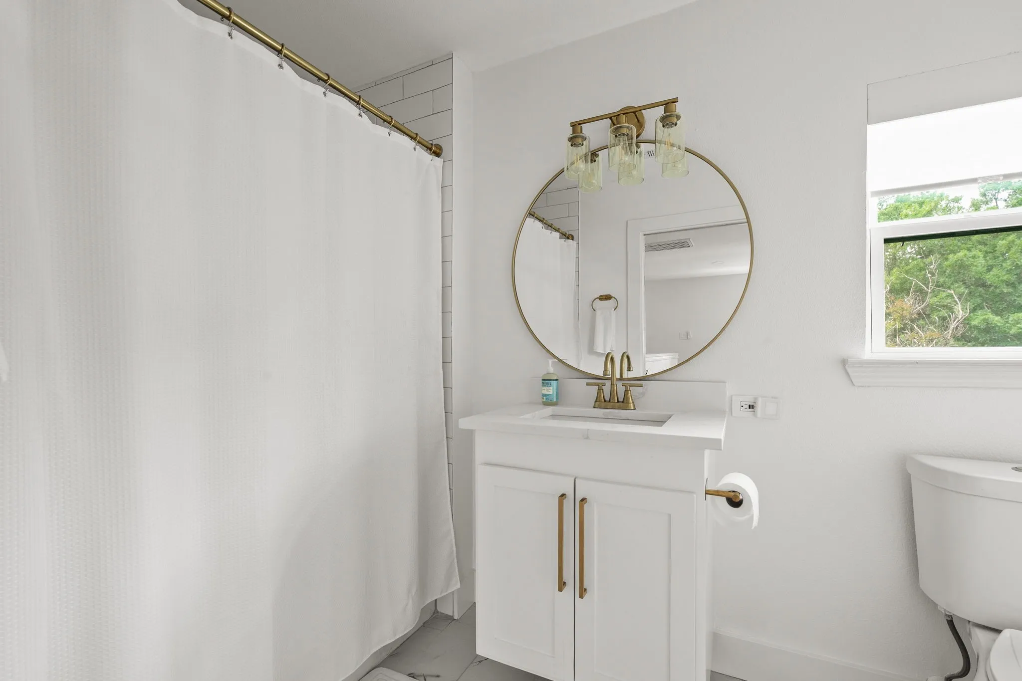 Bathroom featuring a white vanity with gold-finish hardware, a circular gold-framed mirror, and a three-light vanity fixture