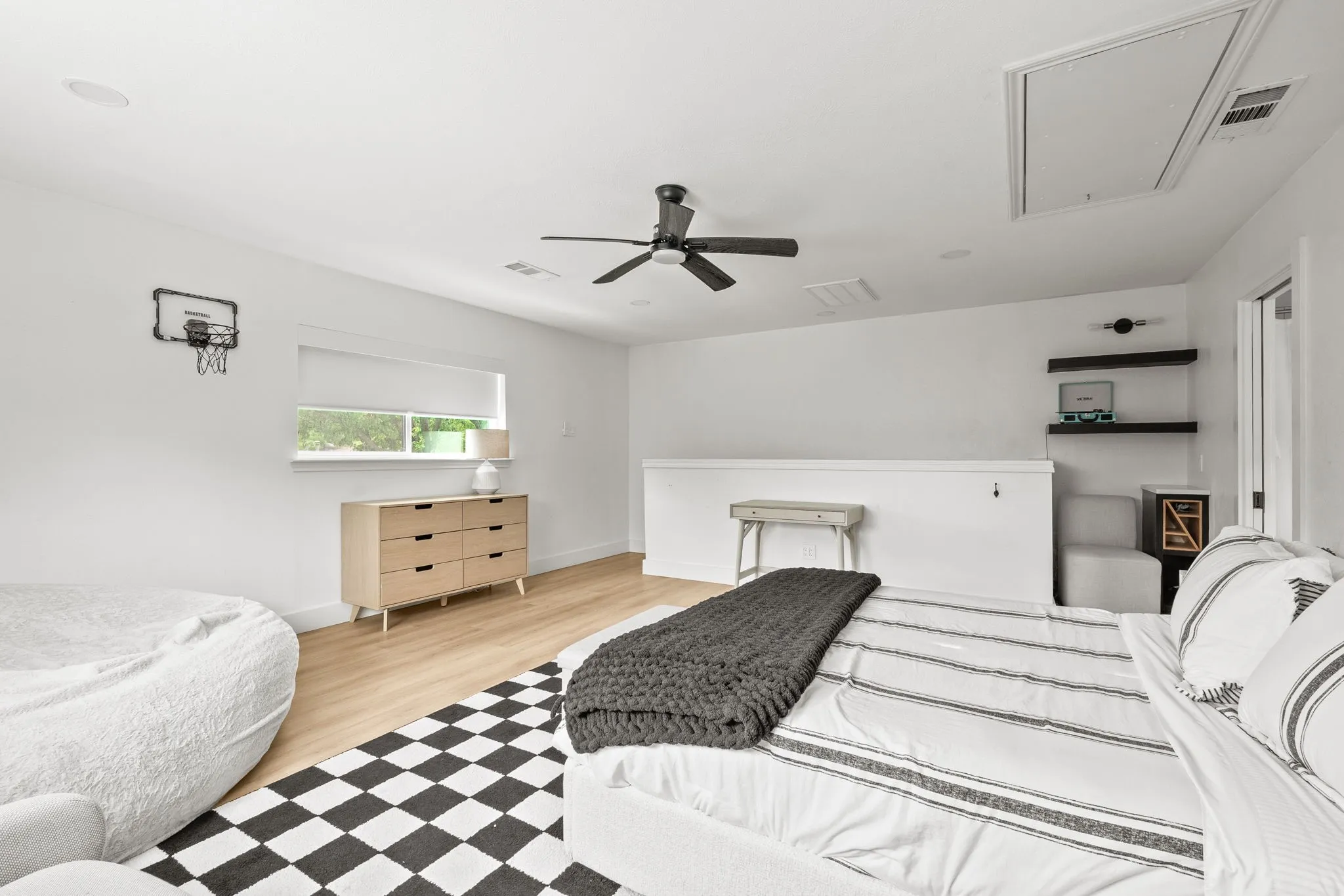 Open loft space featuring light wood-finish flooring, a ceiling fan, recessed lighting, and a window with a roller shade