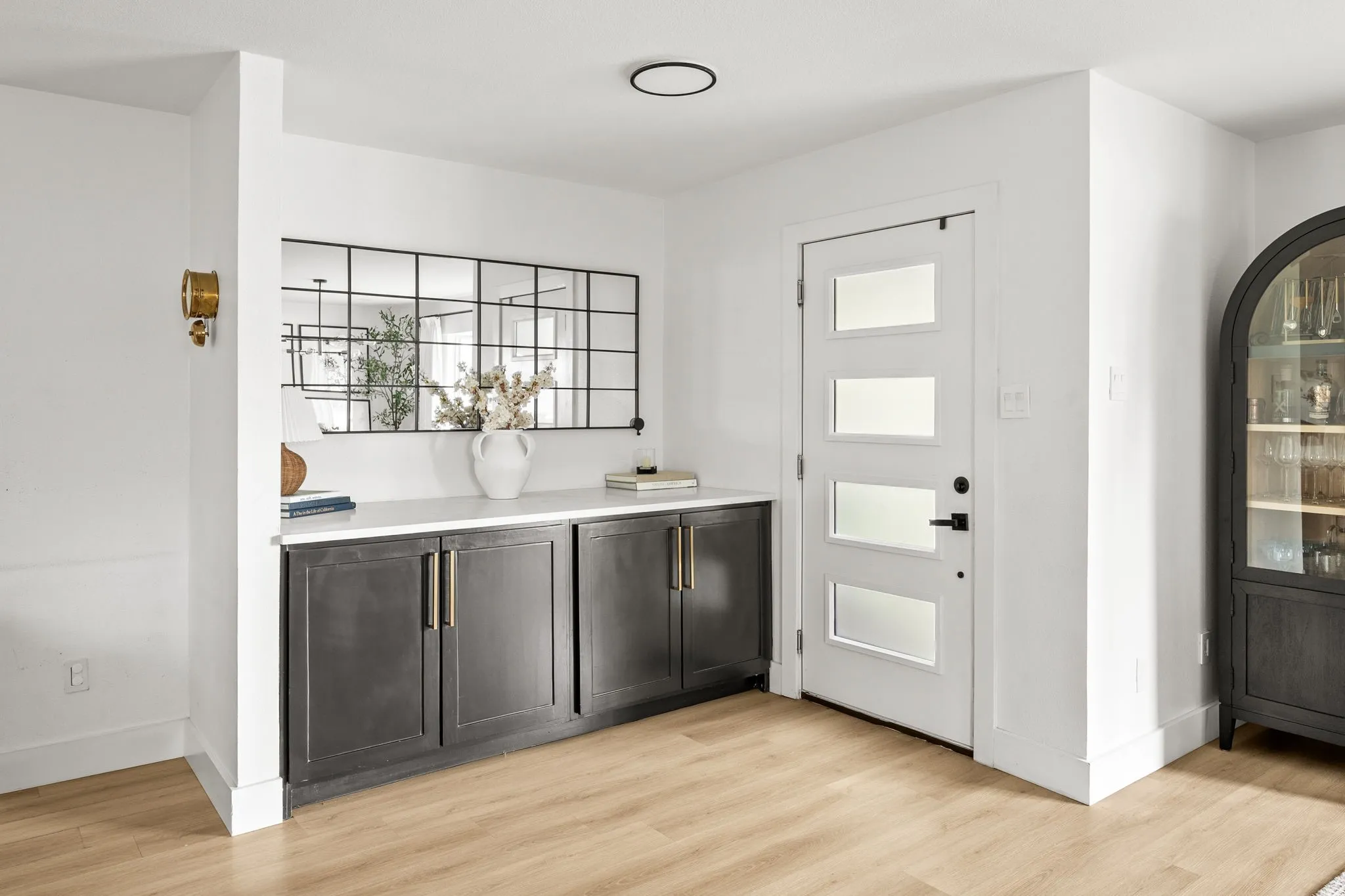 Entryway featuring a white door with frosted glass panels, a built-in dark cabinetry with gold-tone hardware and white countertop, and light wood-finish flooring