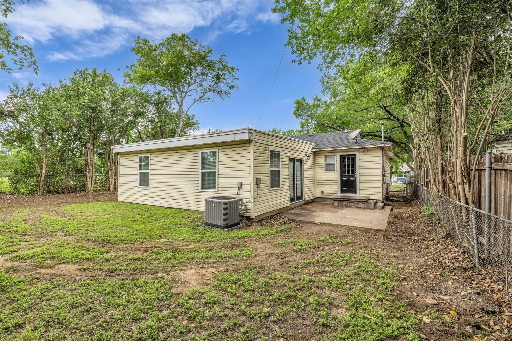Expansive backyard featuring a concrete patio, chain-link fencing, and mature perimeter trees