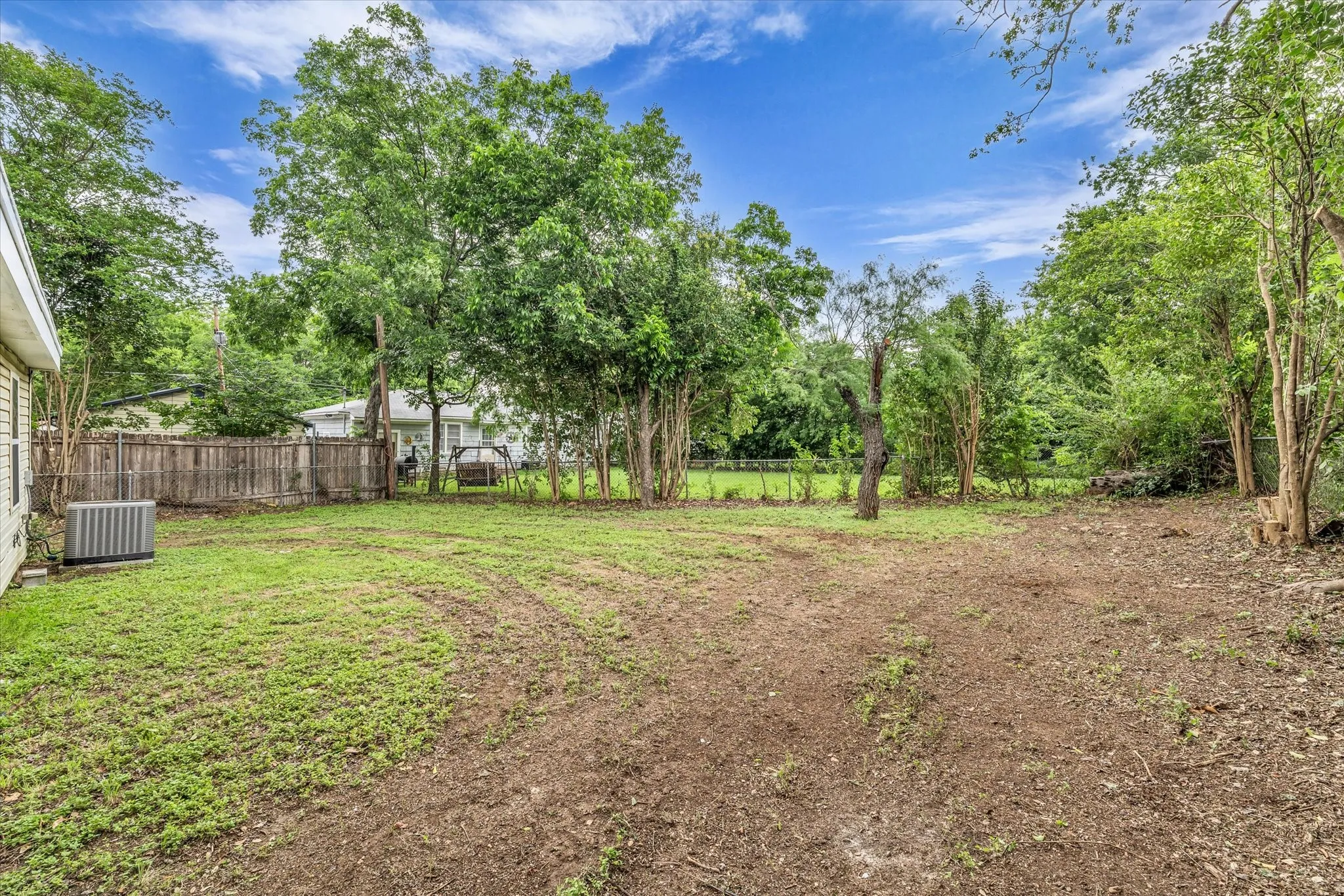 Expansive backyard area featuring a combination of grass and natural ground cover, bordered by mature trees and a wood fence