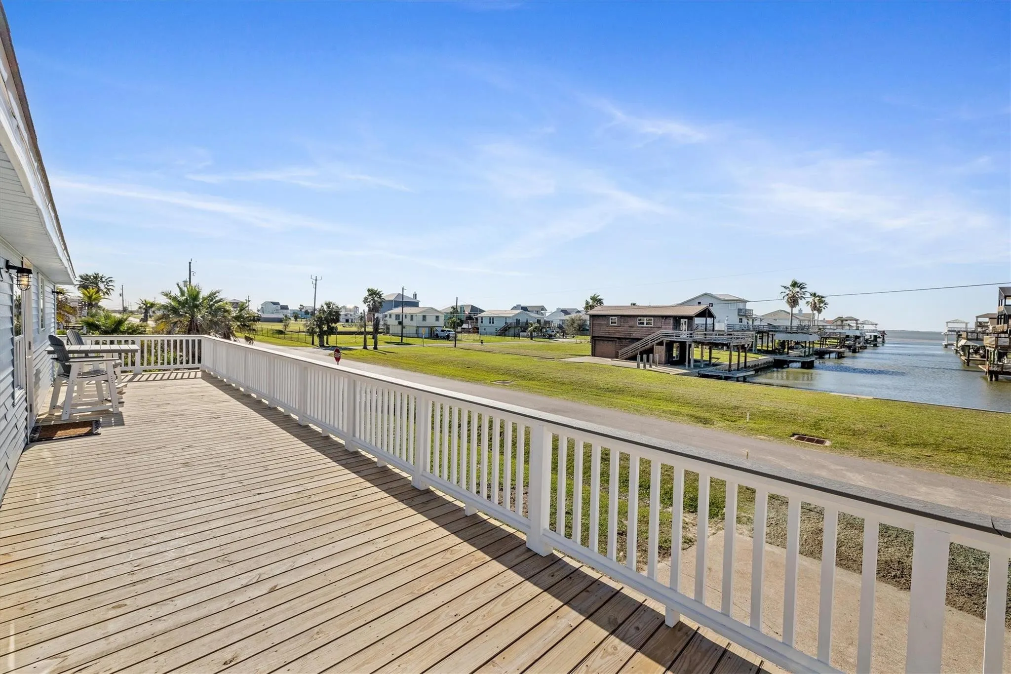 Expansive wood deck with white railing, featuring a waterfront setting with multiple boat slips and distant properties