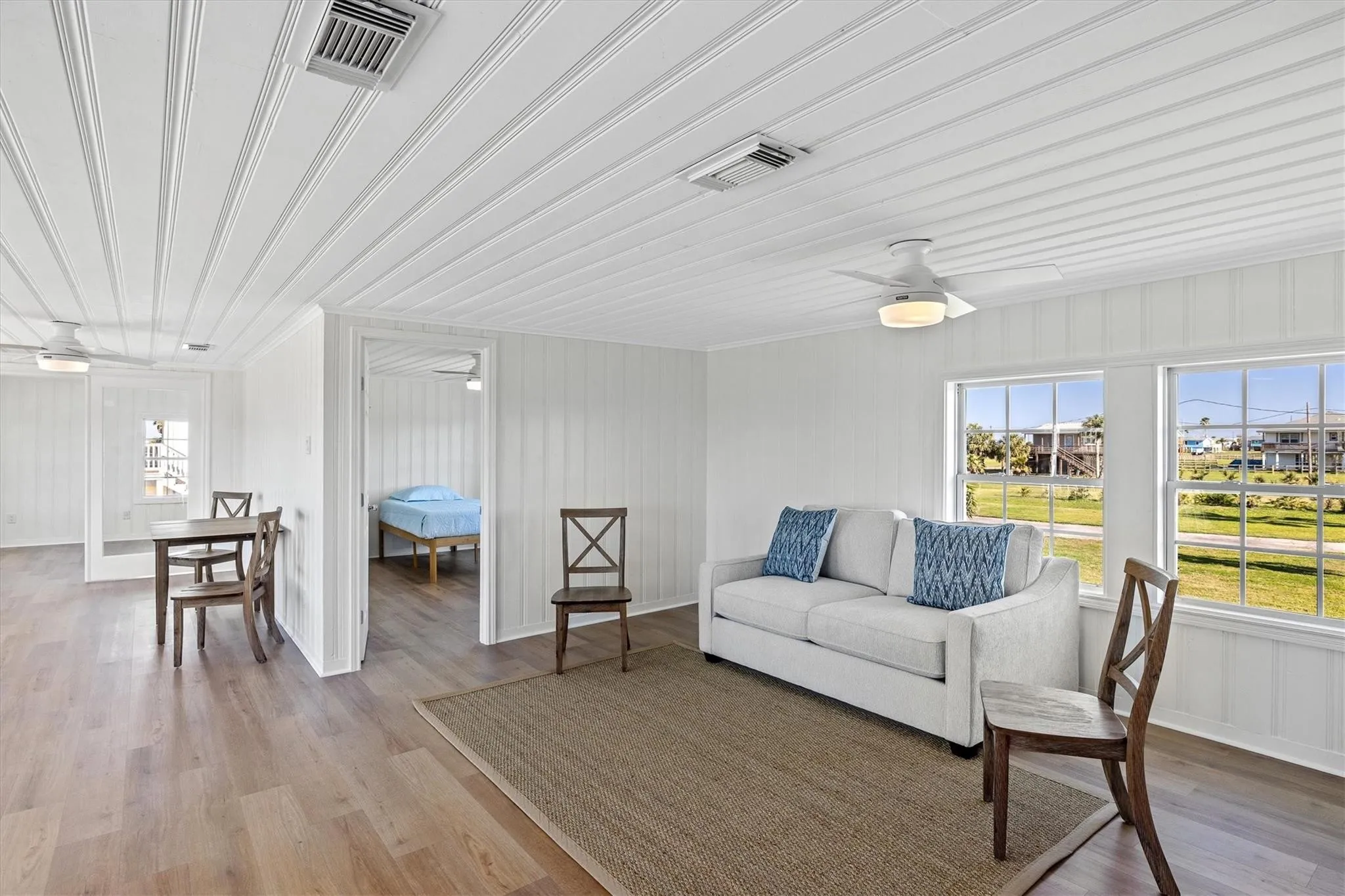 Spacious living area featuring white paneling, wood-finish flooring, and multiple windows providing ambient light