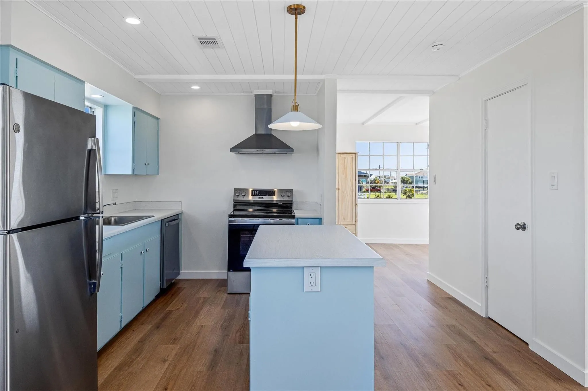 Kitchen featuring wood-finish flooring, light blue cabinetry, stainless steel appliances, a center island with a white countertop, and a white plank ceiling