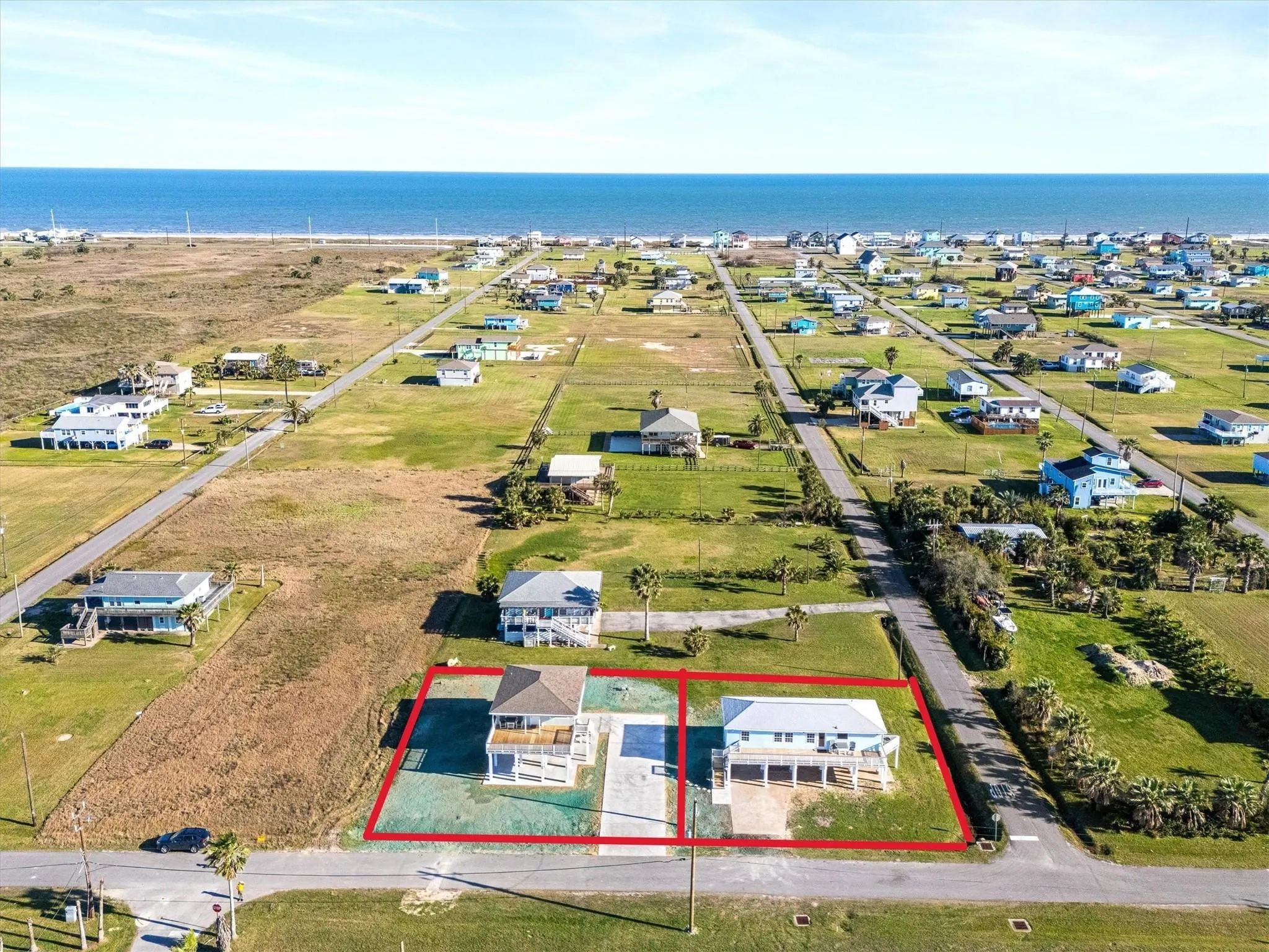 Coastal property featuring two raised residences, each with a ground-level concrete pad and a private driveway