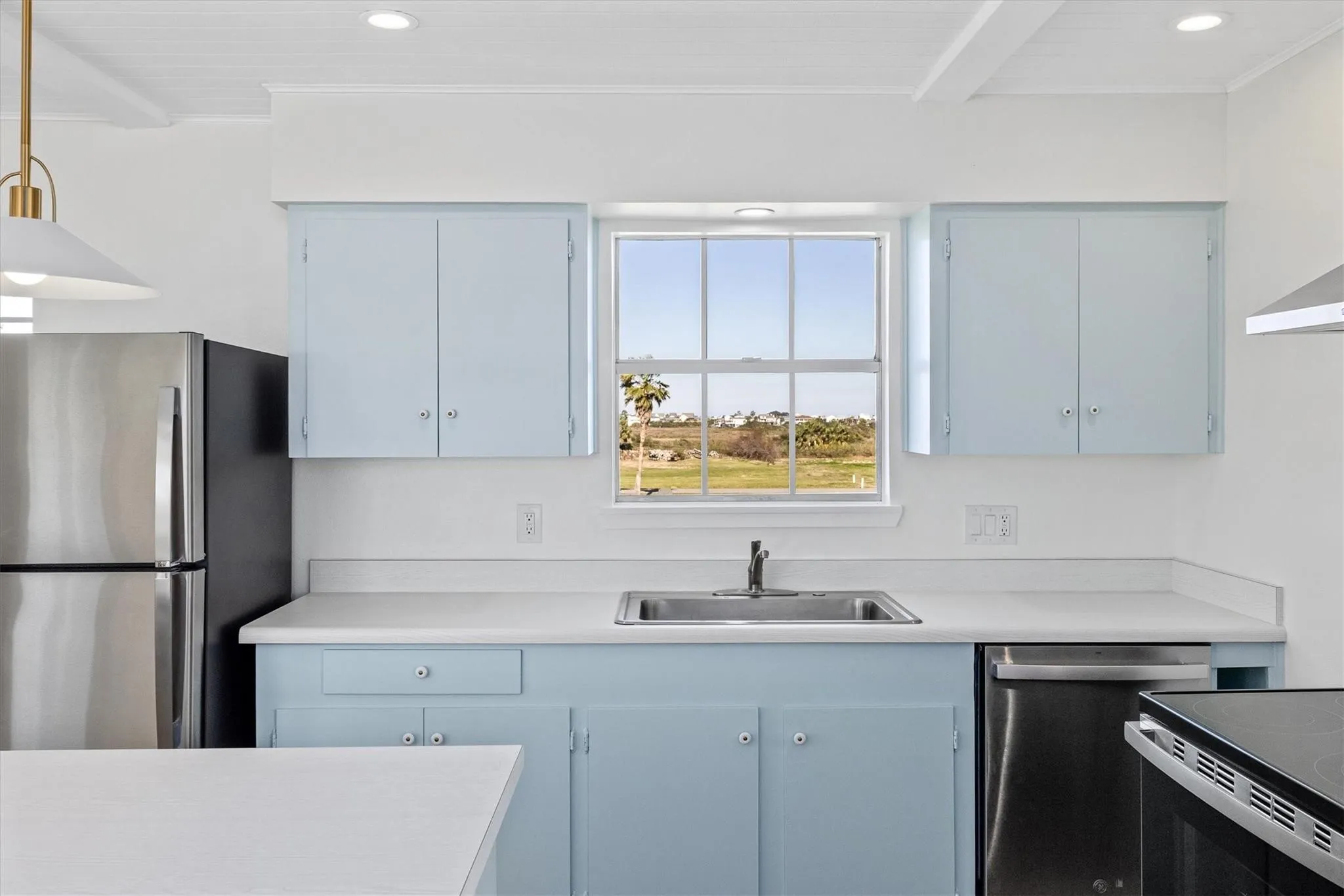 Kitchen featuring light blue cabinetry, white countertops, stainless steel sink, and a window overlooking a landscape