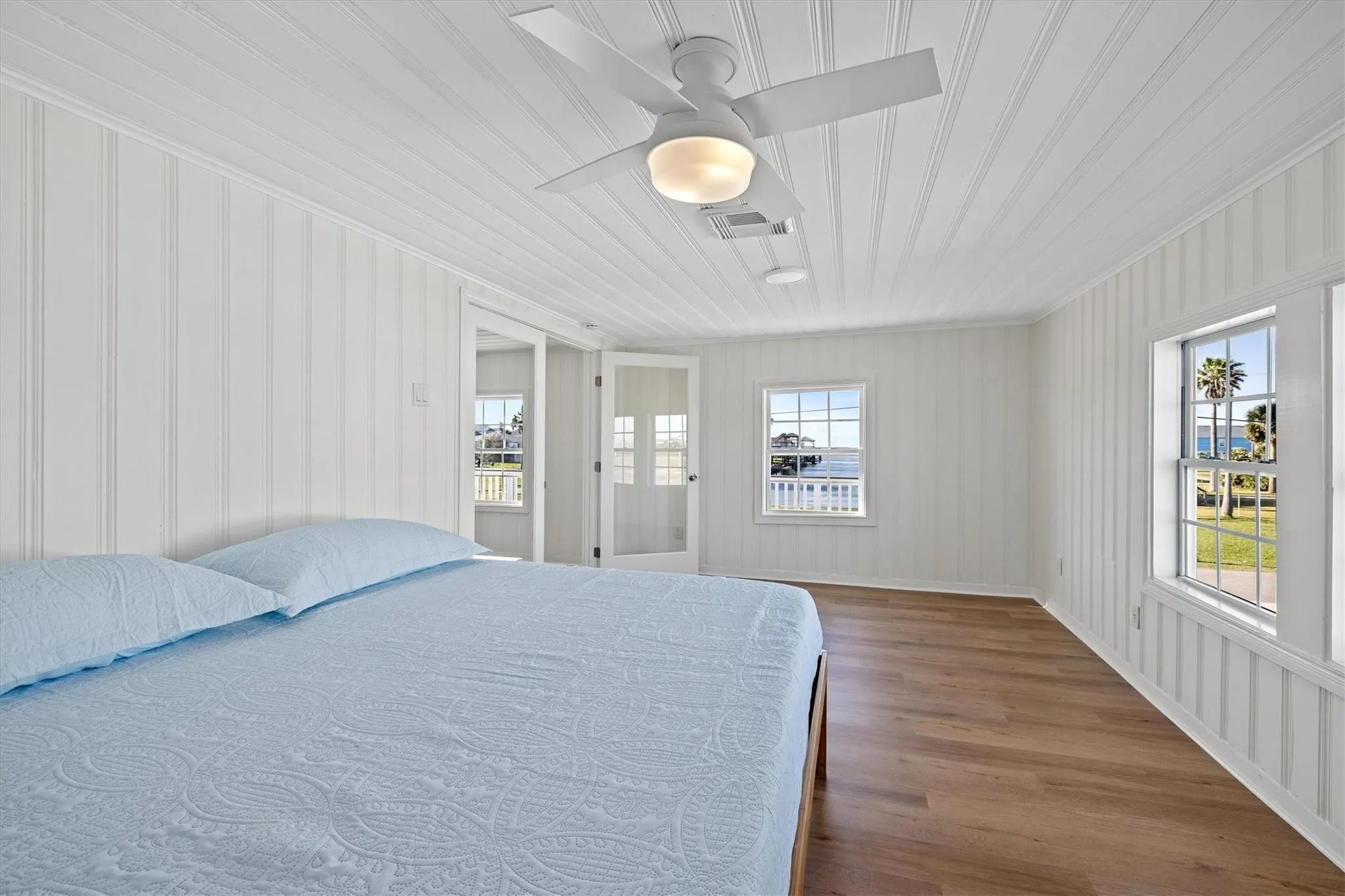 Spacious room featuring white vertical plank walls, a matching planked ceiling, wood-finish flooring, and multiple windows