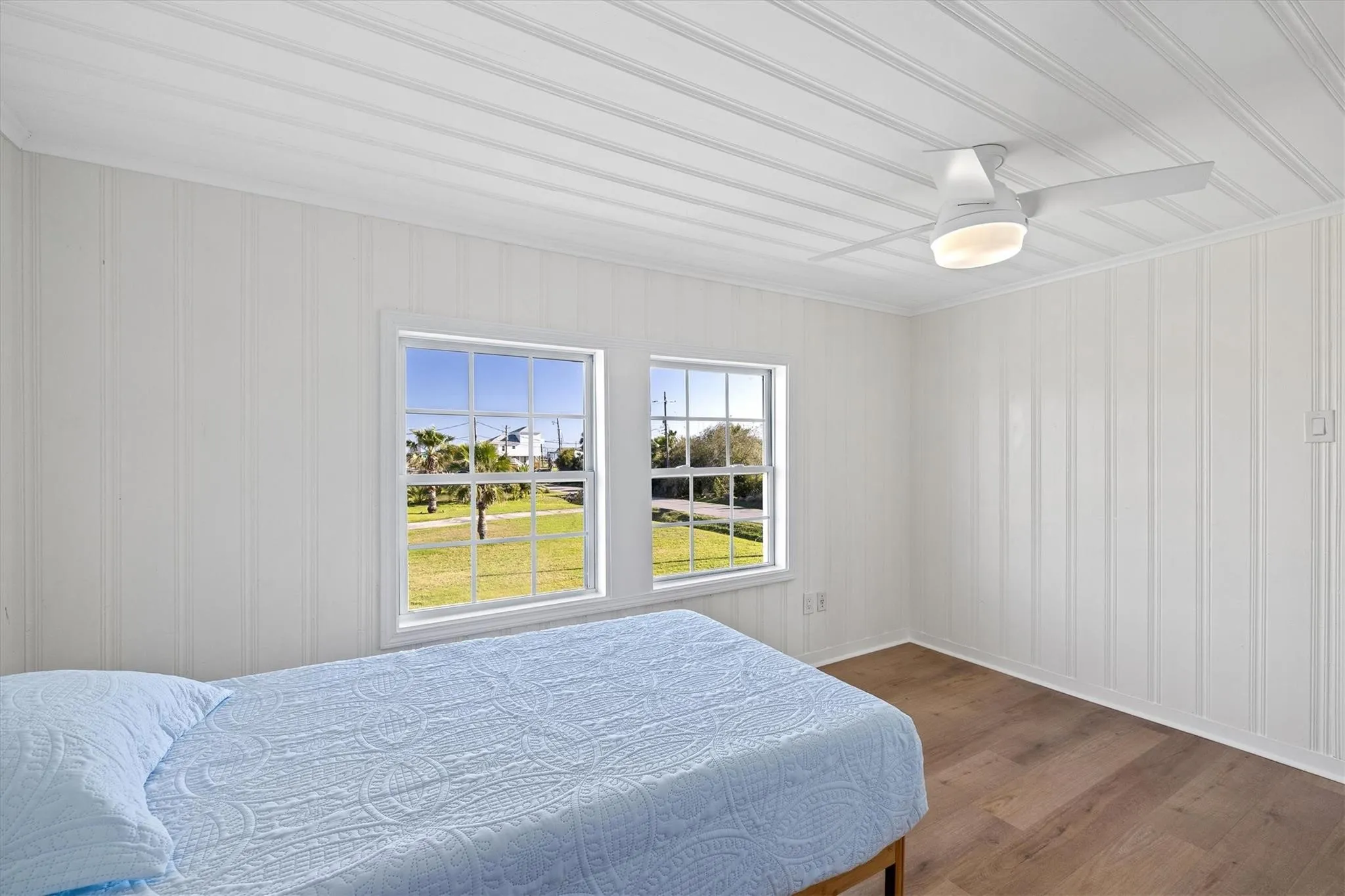 Interior room featuring two multi-pane windows, wood-finish flooring, and white vertical paneling