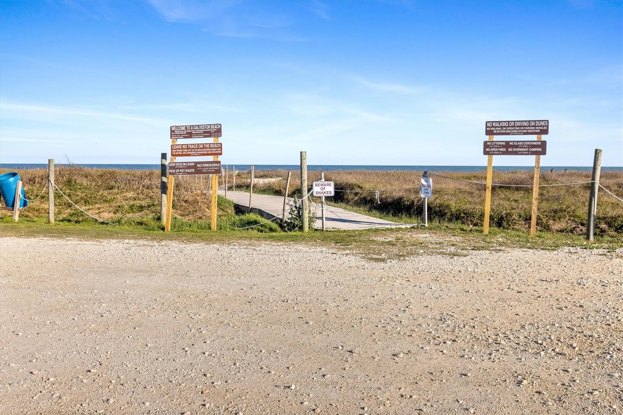 Beach access point featuring a wooden boardwalk leading to the water, natural dune vegetation, and a clear blue sky