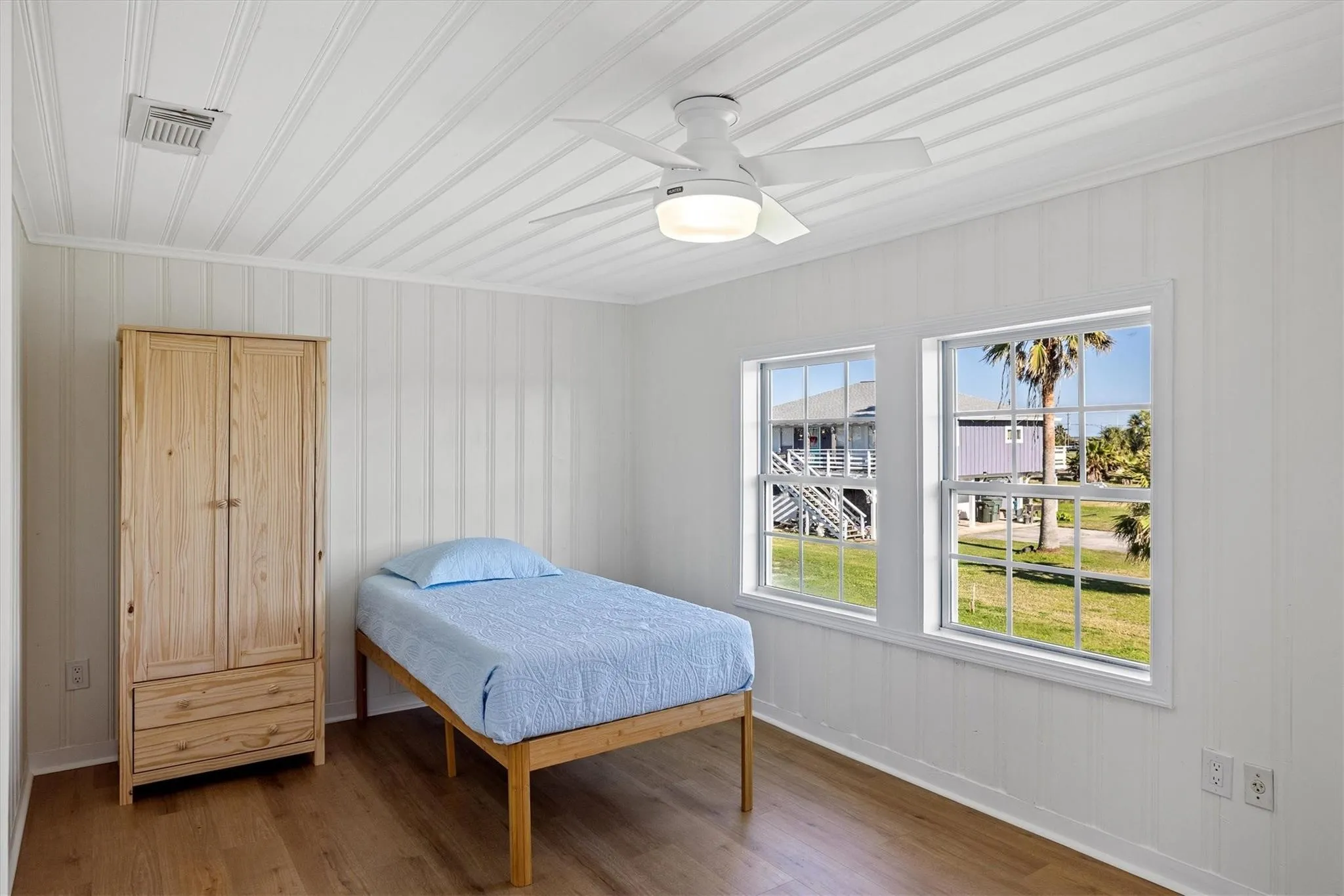 Room featuring two large windows, wood-finish flooring, and white beadboard paneling on walls and ceiling