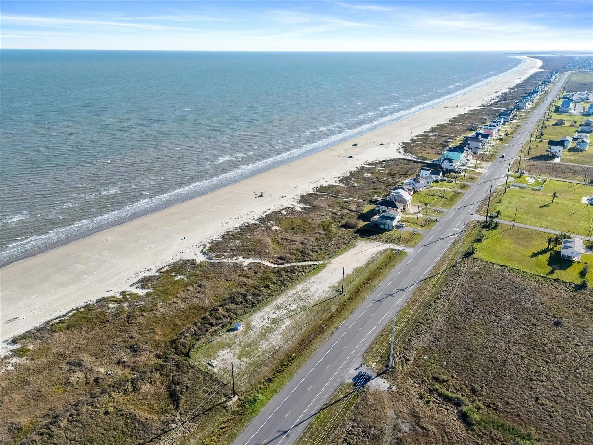 Expansive coastal setting featuring beachfront properties, a paved roadway, and open land areas