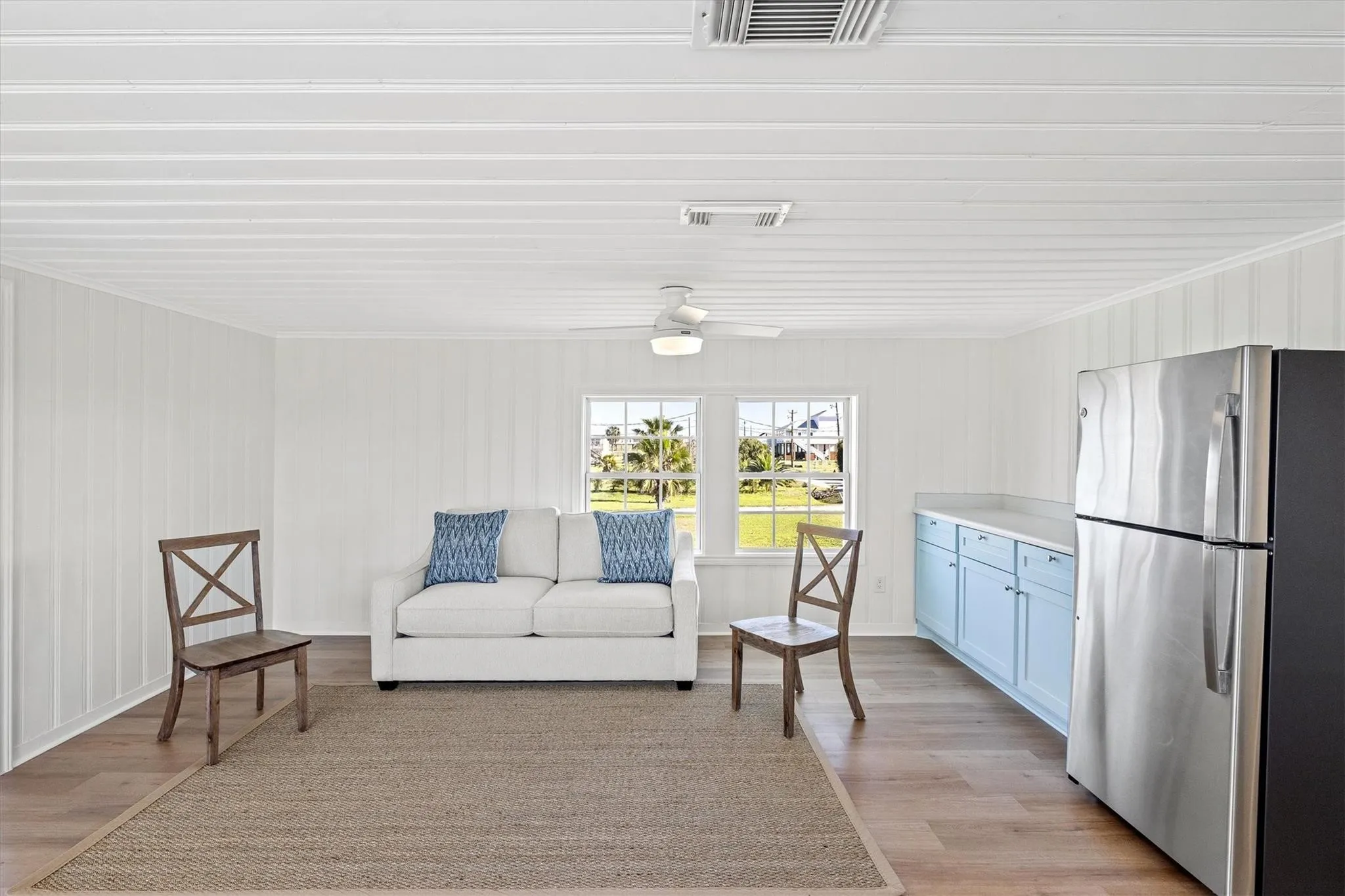 Open-concept living area featuring white shiplap walls, wood-finish flooring, and a ceiling fan