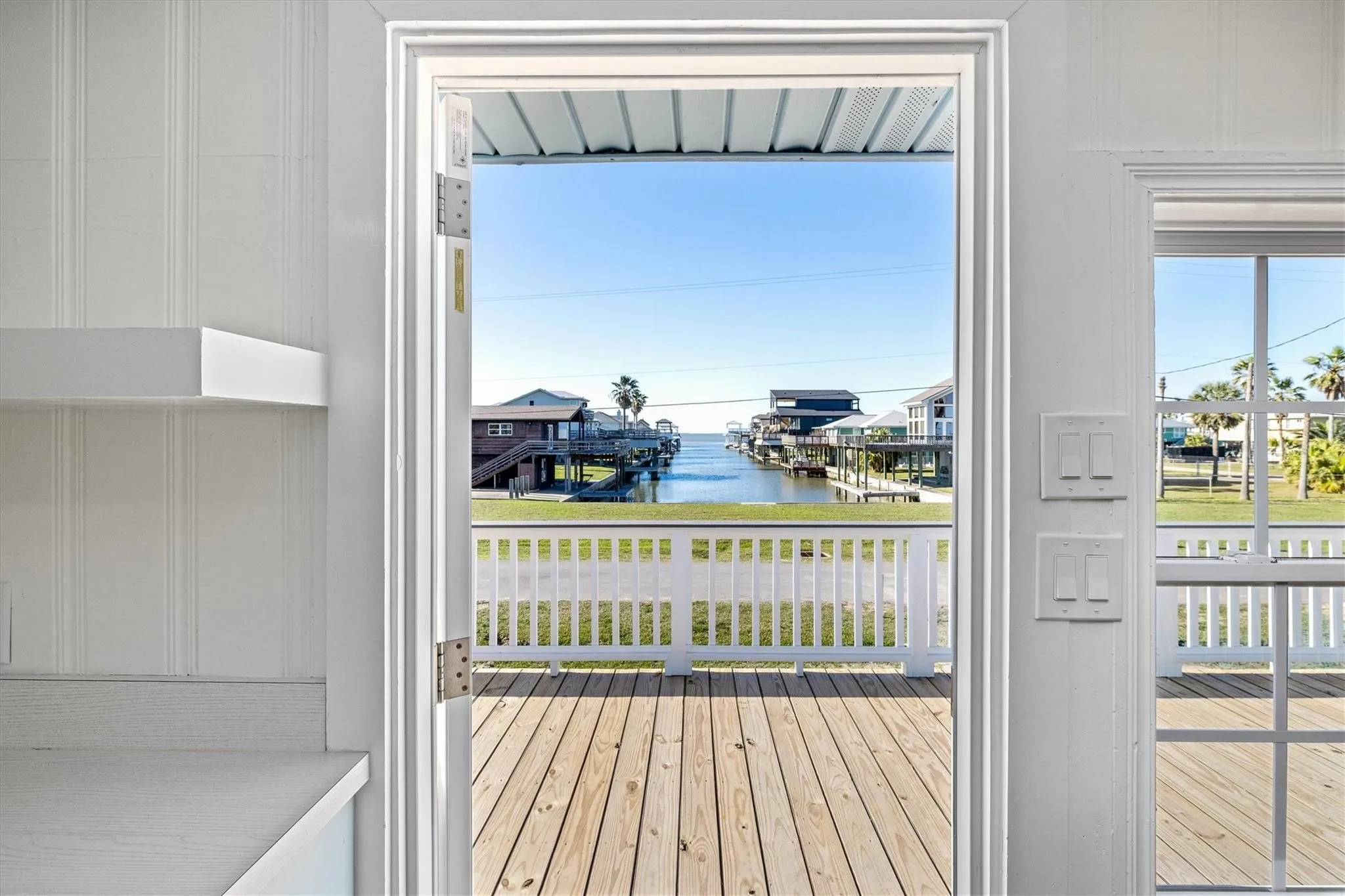 Outdoor deck featuring wood-finish flooring and a white railing, overlooking a canal with multiple properties