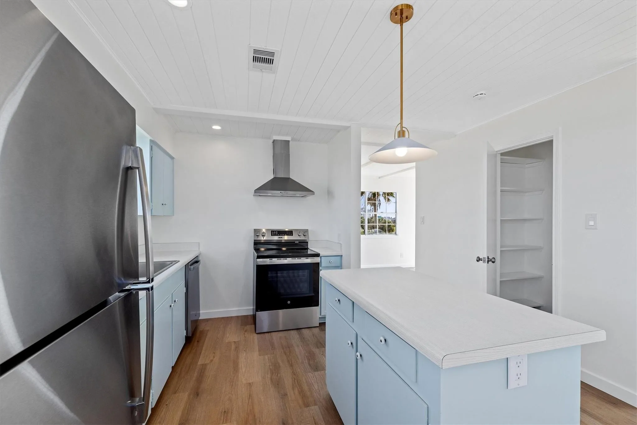 Kitchen featuring a central island with light blue cabinetry, light-toned countertops, stainless steel appliances, and wood-finish flooring