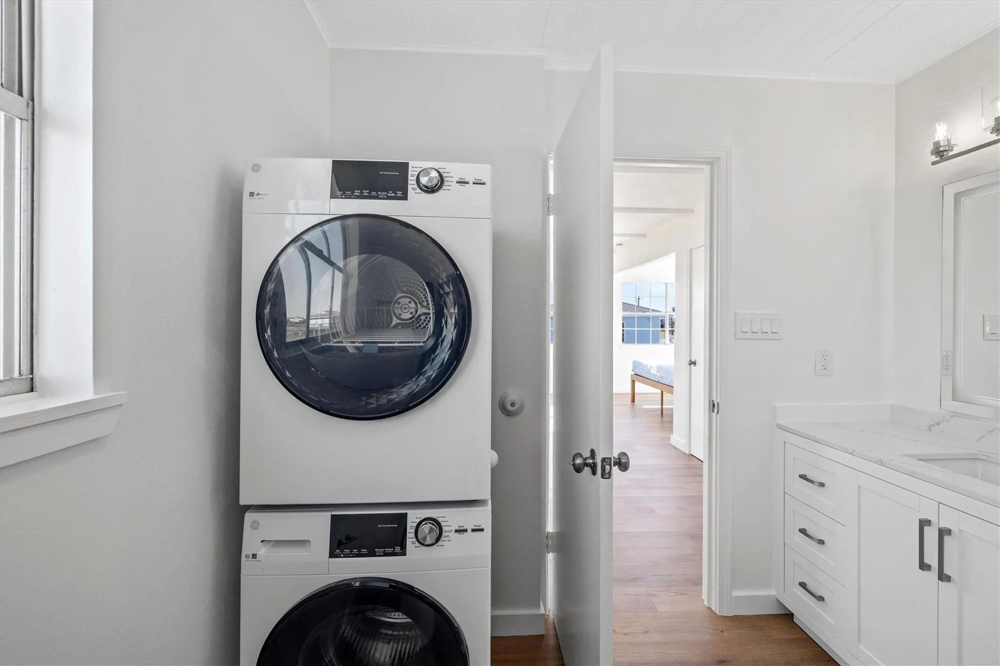 Laundry area featuring a stacked washer and dryer, adjacent to a bathroom vanity with a white countertop and white cabinetry
