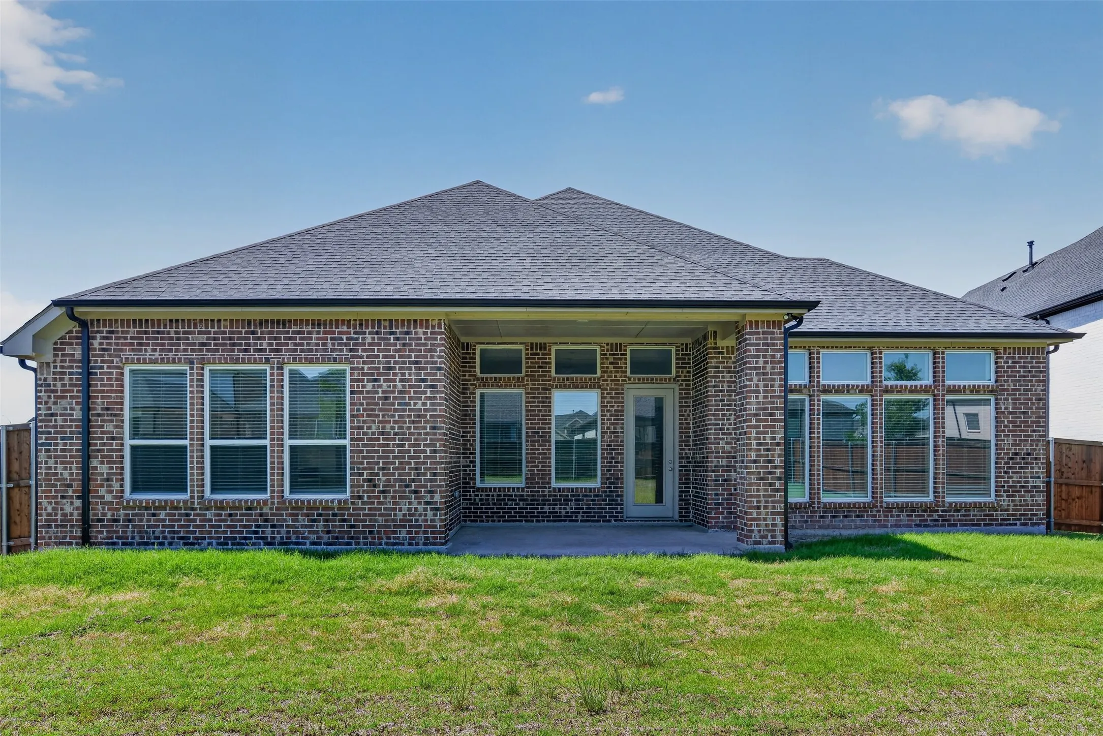 Brick exterior featuring a covered patio, multiple large windows, and a glass-paneled door