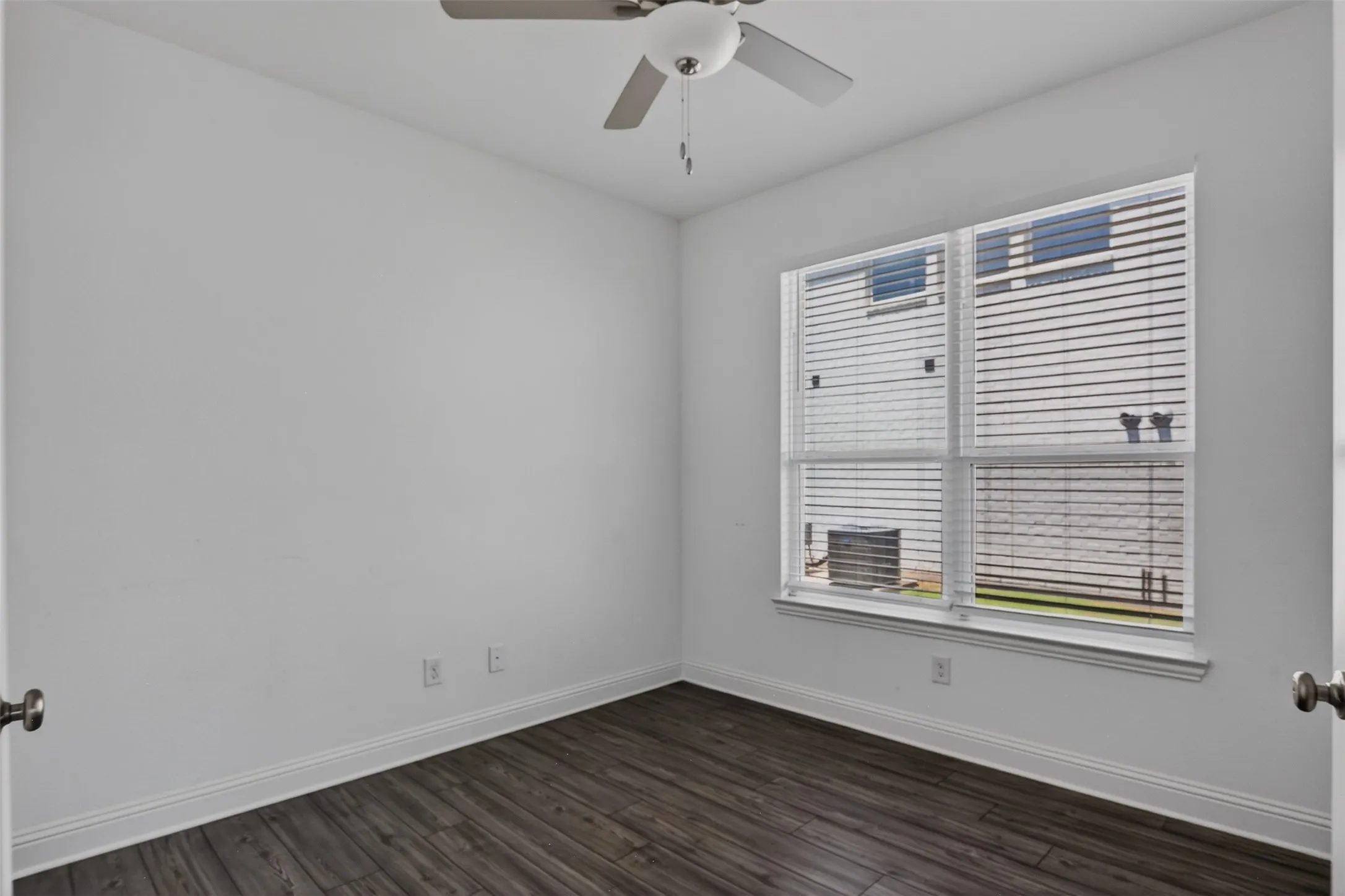 Bright room featuring wood-finish flooring, white baseboards, a ceiling fan with light fixture, and a large window with blinds