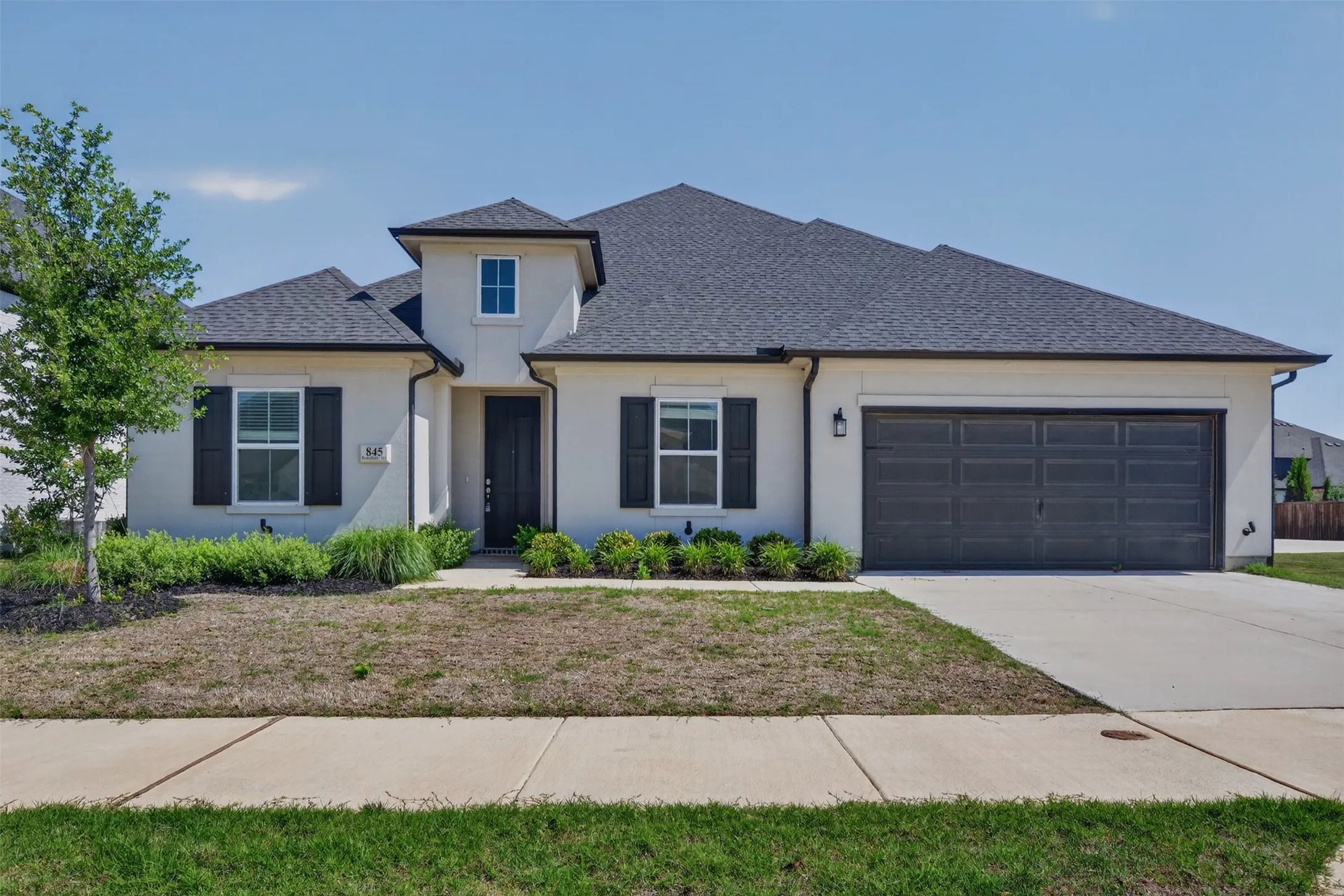 Stucco exterior featuring a dark asphalt shingle roof, black decorative shutters, and an attached two-car garage with a dark panel door